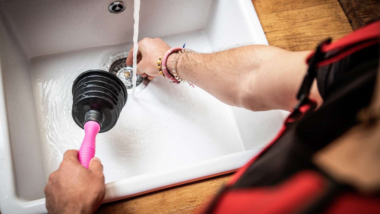 A plumber unclogging a kitchen sink using a plunger