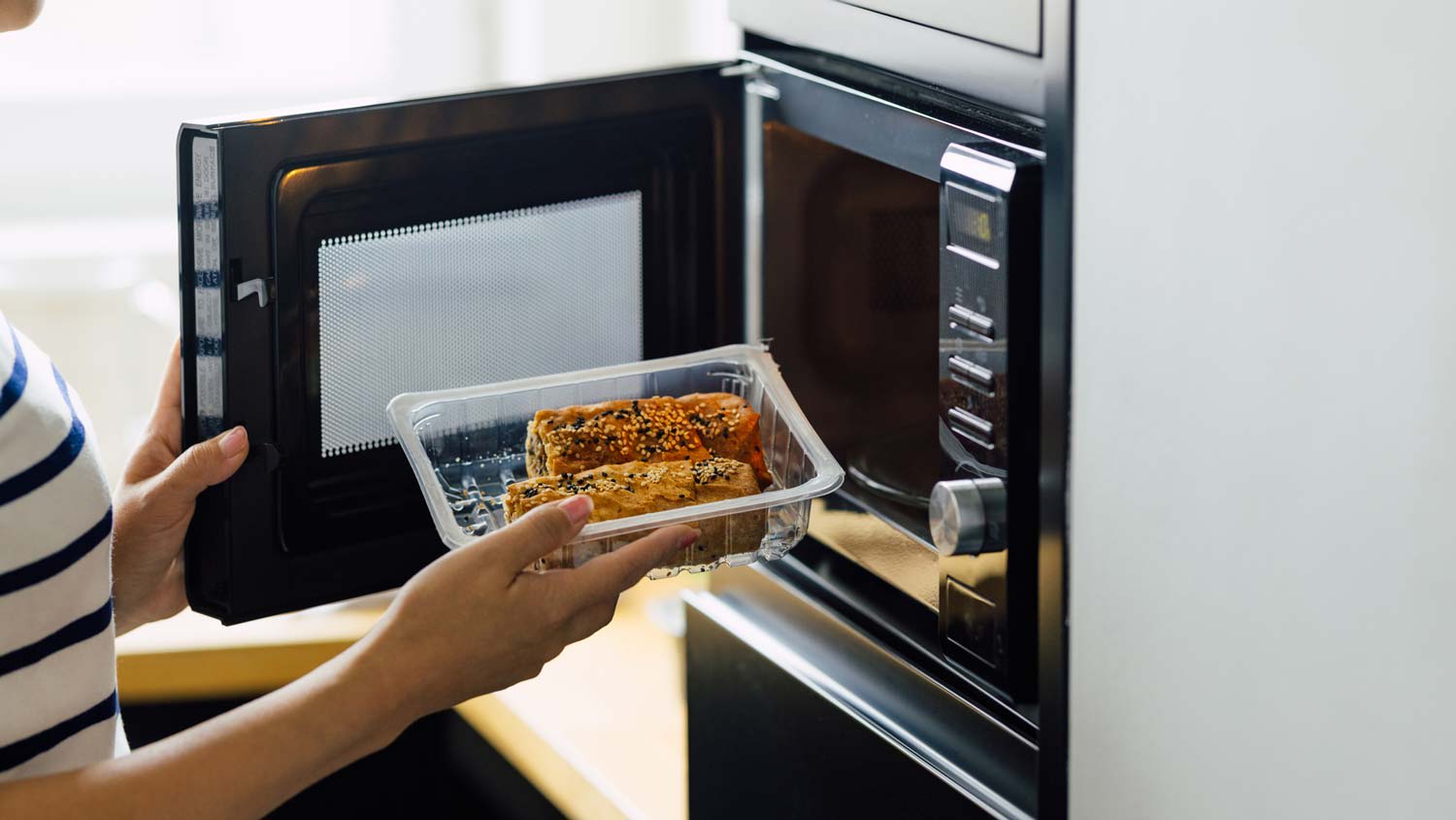 A woman placing food in a microwave oven