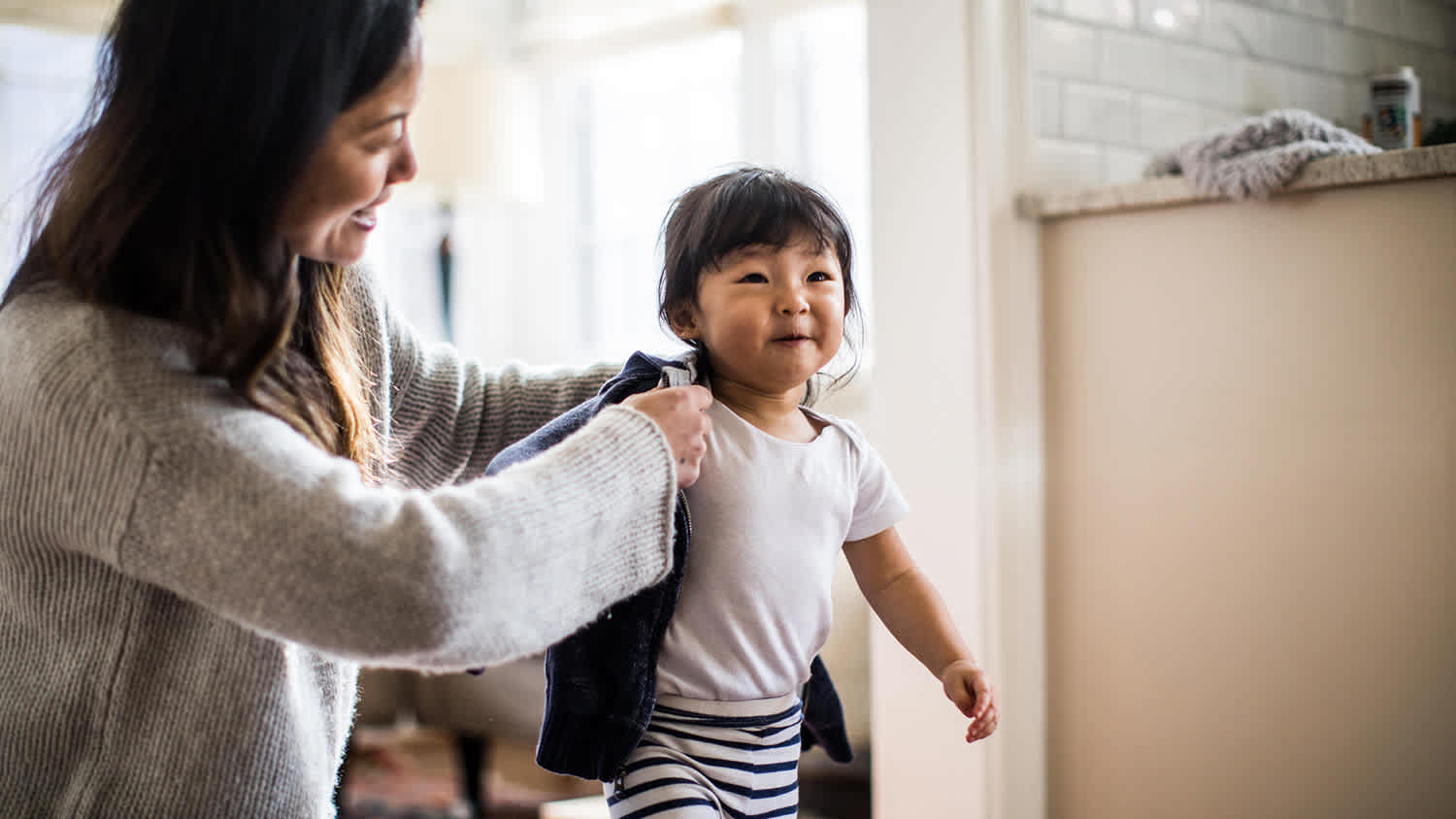 Mother helping toddler put on sweater in house