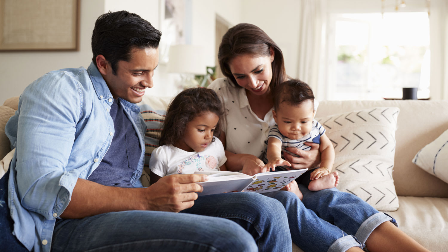 A family of four seating on the sofa reading a book