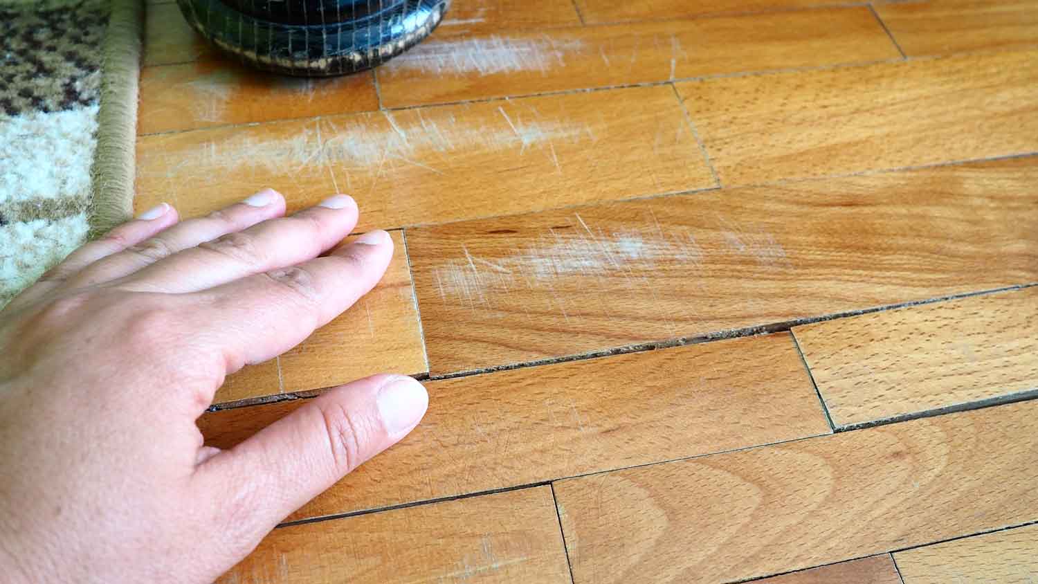 A person inspecting a hardwood floor with scratches and gaps