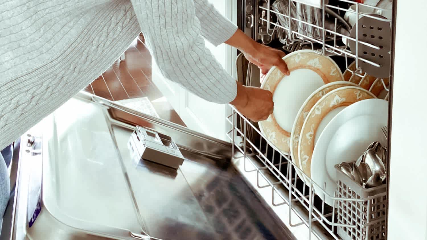Close-up of a woman’s hand placing plates into dishwasher