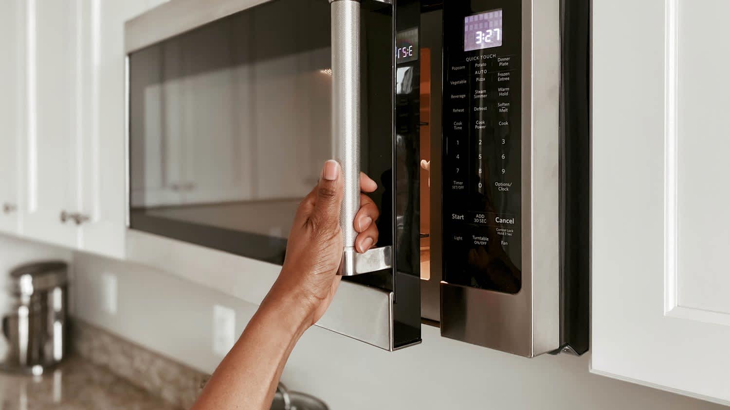 A woman opening a microwave door
