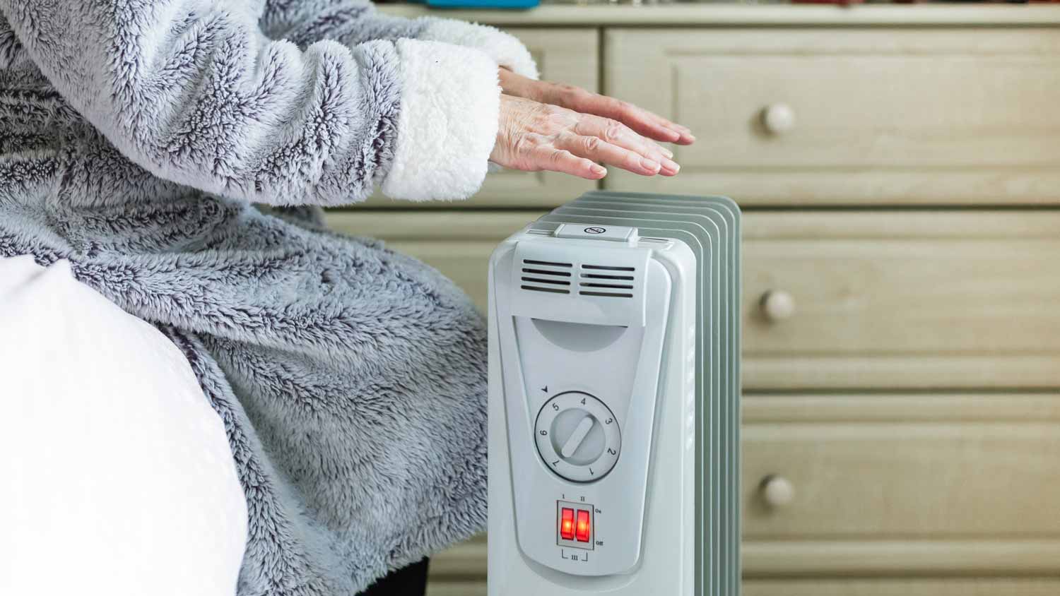 A senior woman warming her hands in front of a space heater