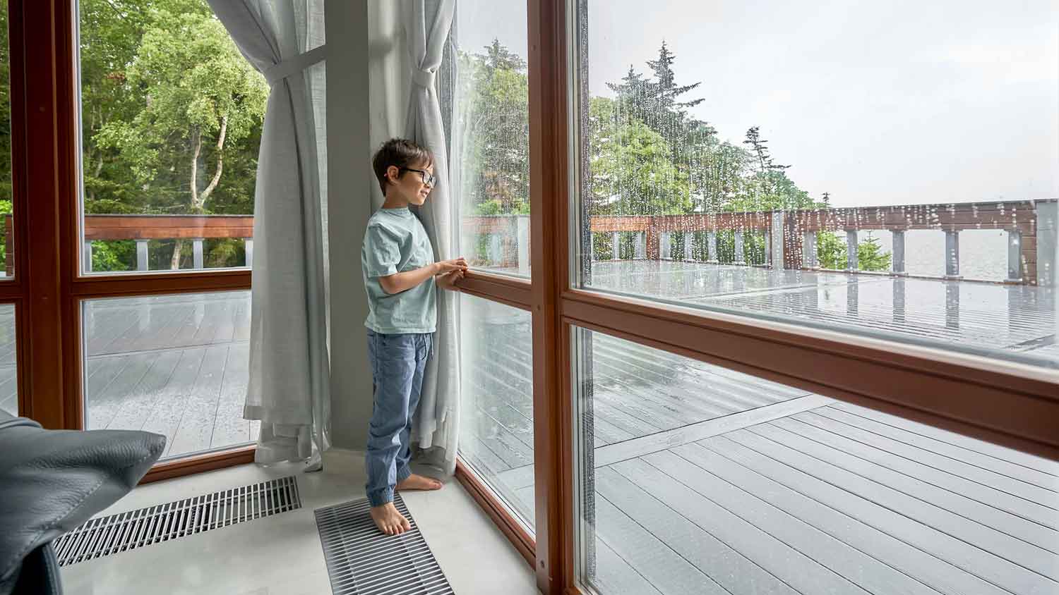 Boy at home watching the rain from the window
