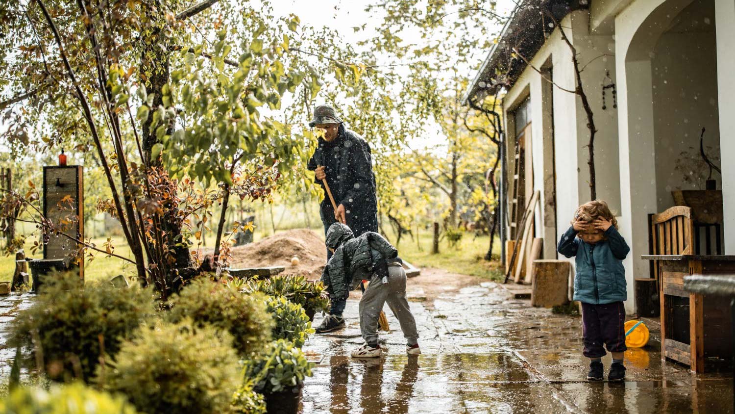 A father sweeping water from patio with two young children