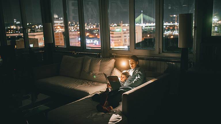 A mother reads to her son in the living room at night