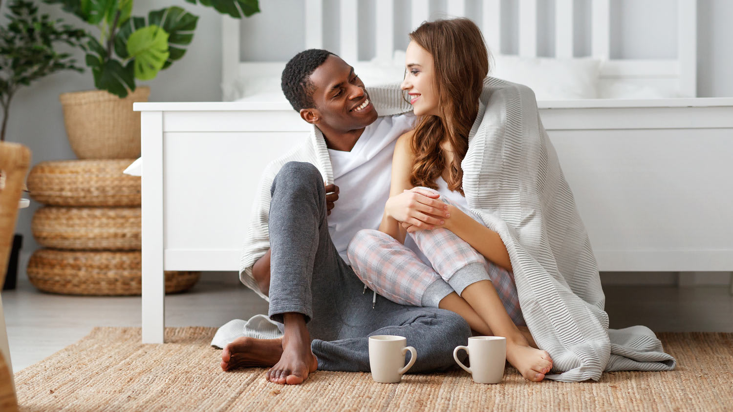 A young couple covered in a blanket enjoying their morning coffee