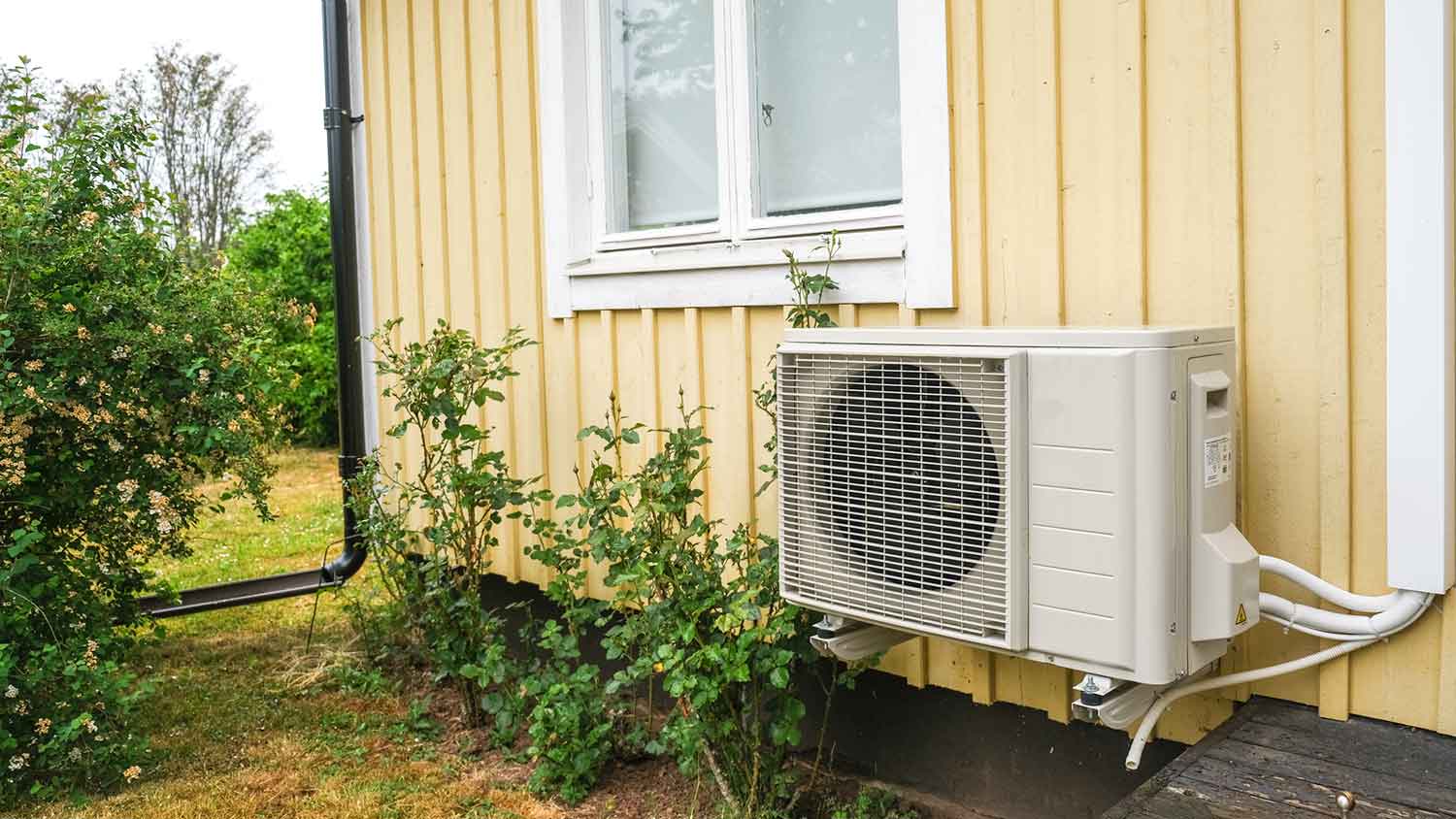Heat pump installed outside of a yellow house