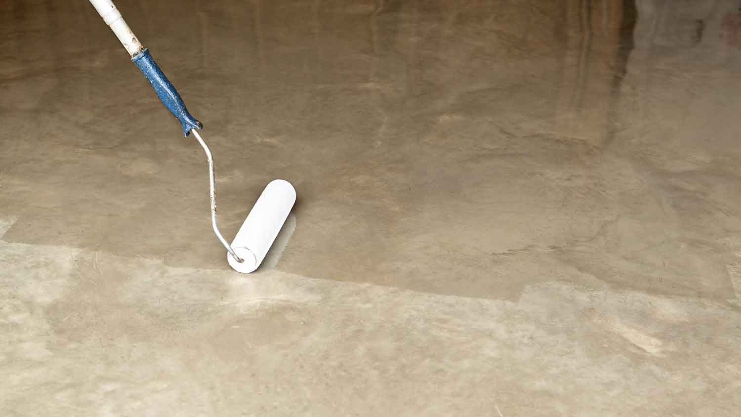 Worker applying concrete sealer with a roller
