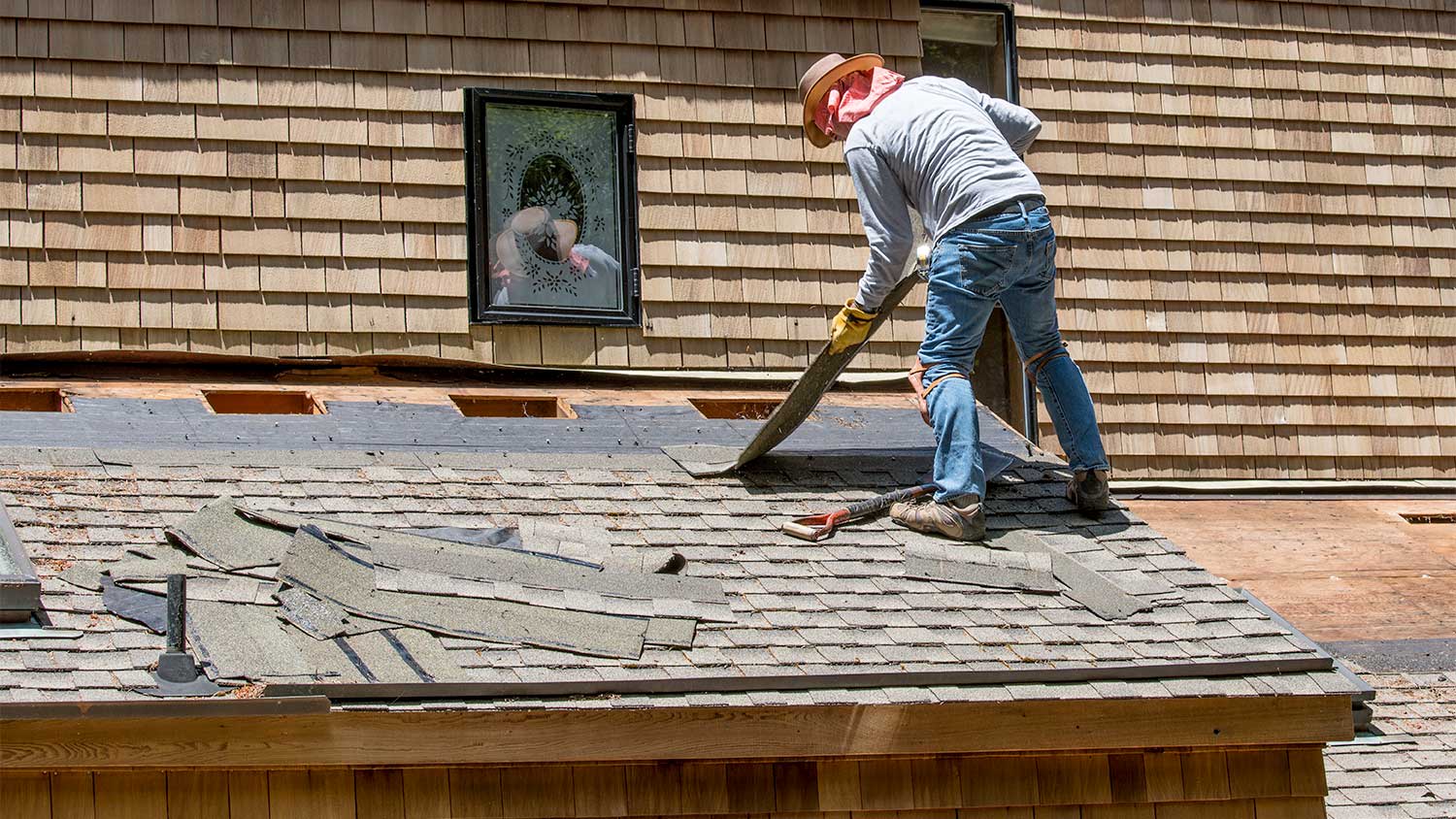 A man removes asphalt shingles from a roof