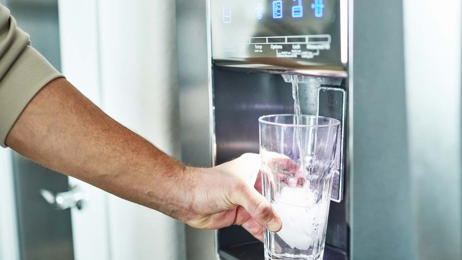 A person pouring in a glass from a fridge water dispenser