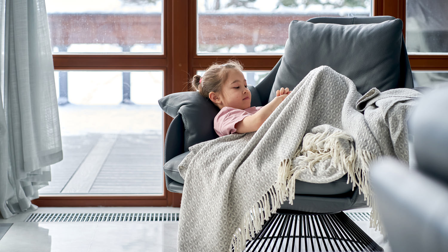 The girl lies under a blanket on an armchair