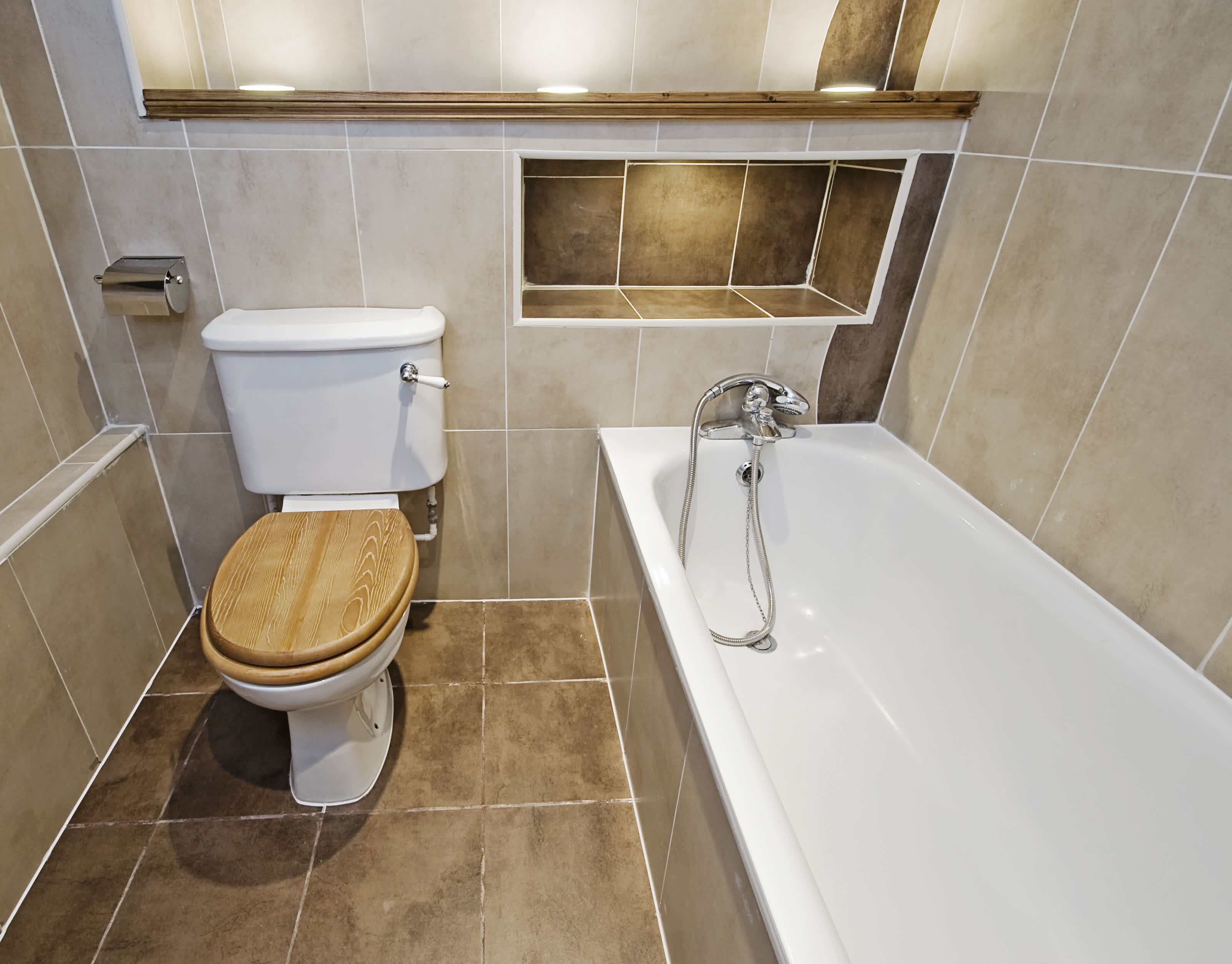 Brown tile bathroom with built-in shower shelves above tub