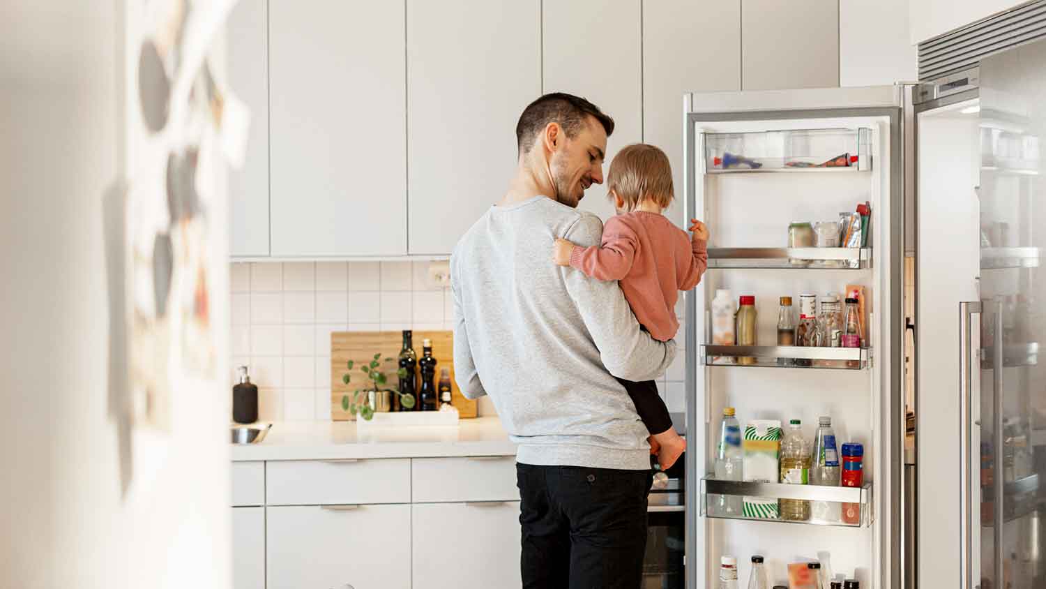 Dad opening fridge and holding toddler daughter