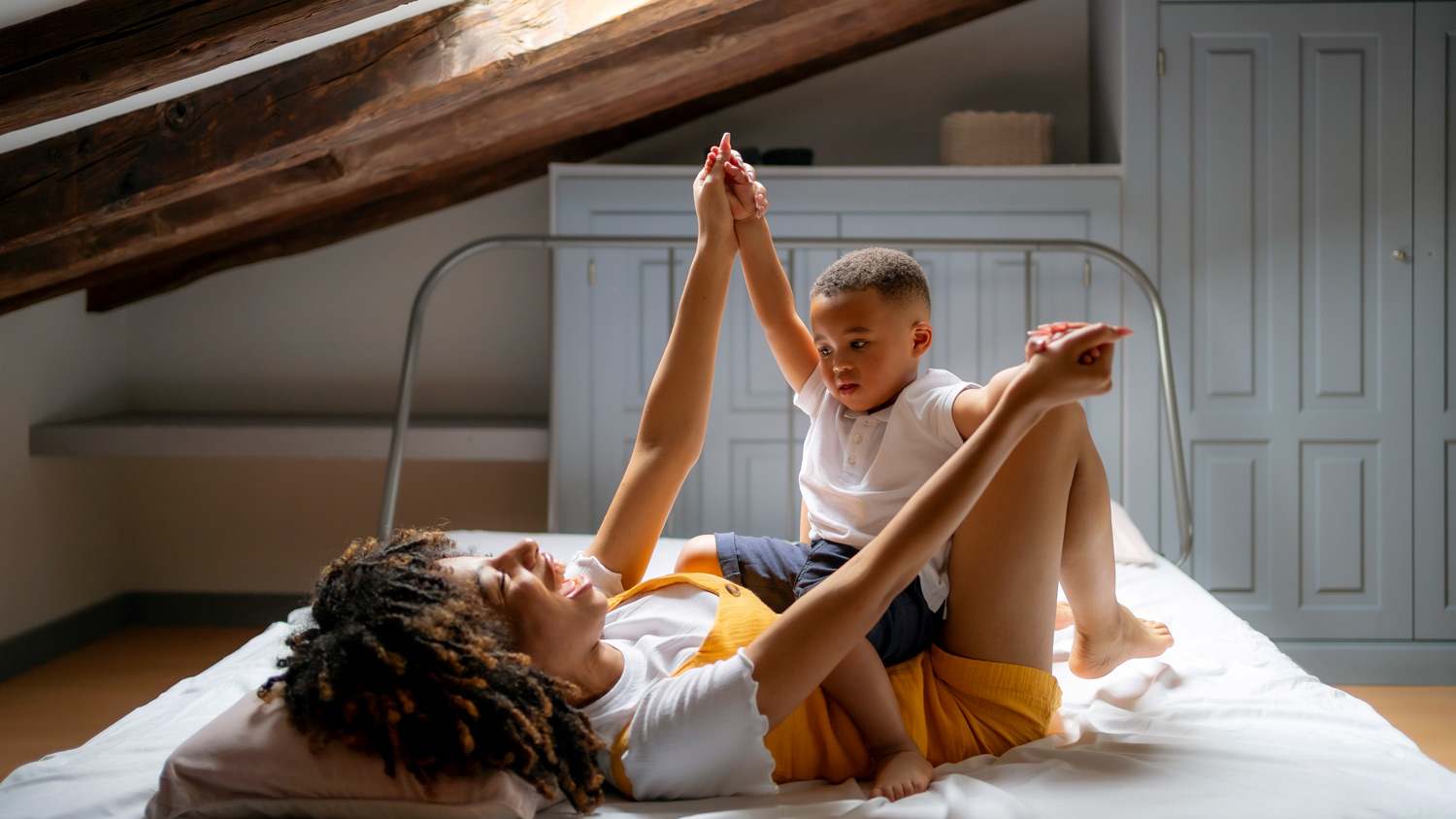 Happy mother playing with son while lying on bed in attic at home