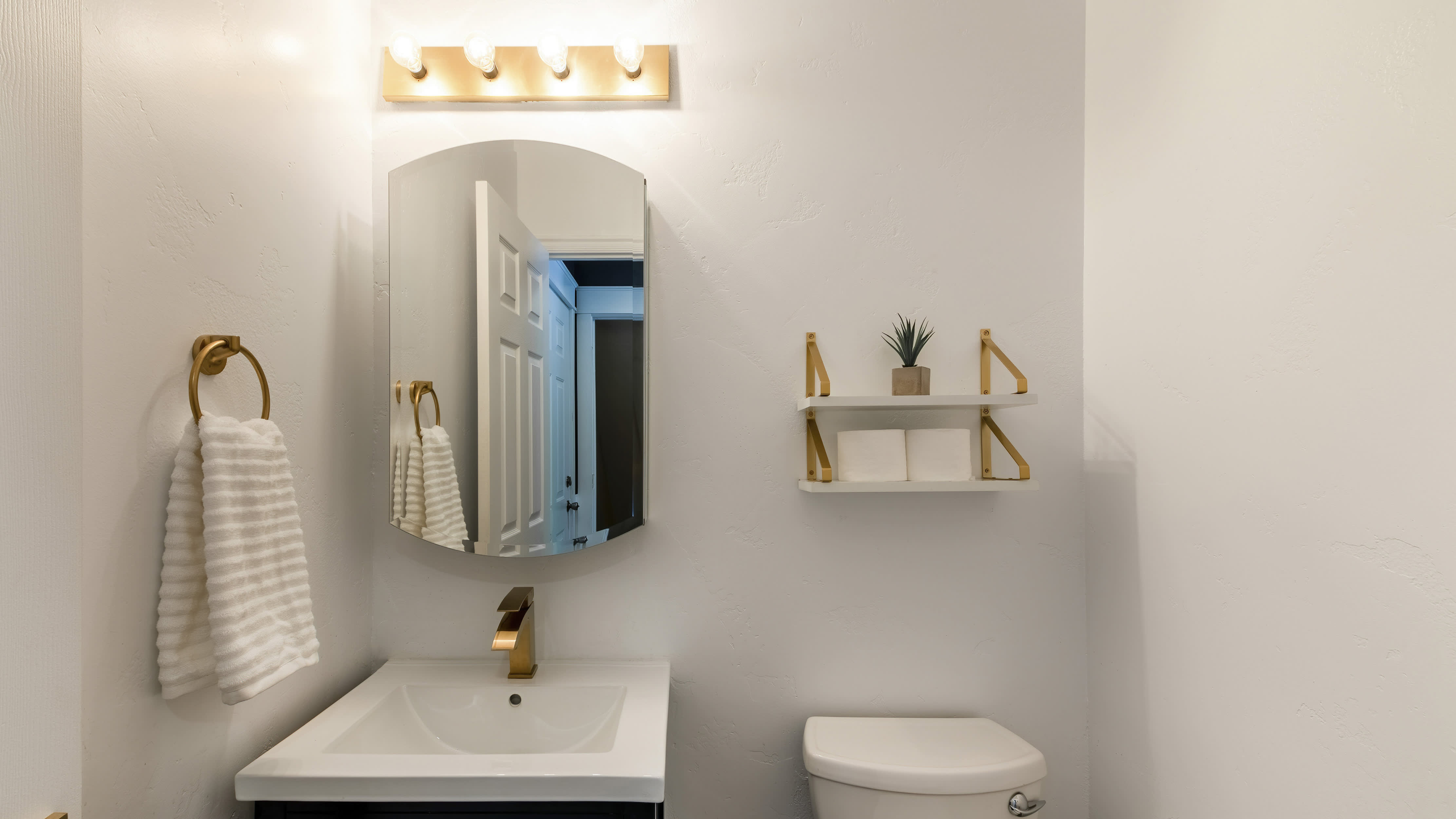 Small powder room with matching gold faucet, towel ring, and open-concept shelf