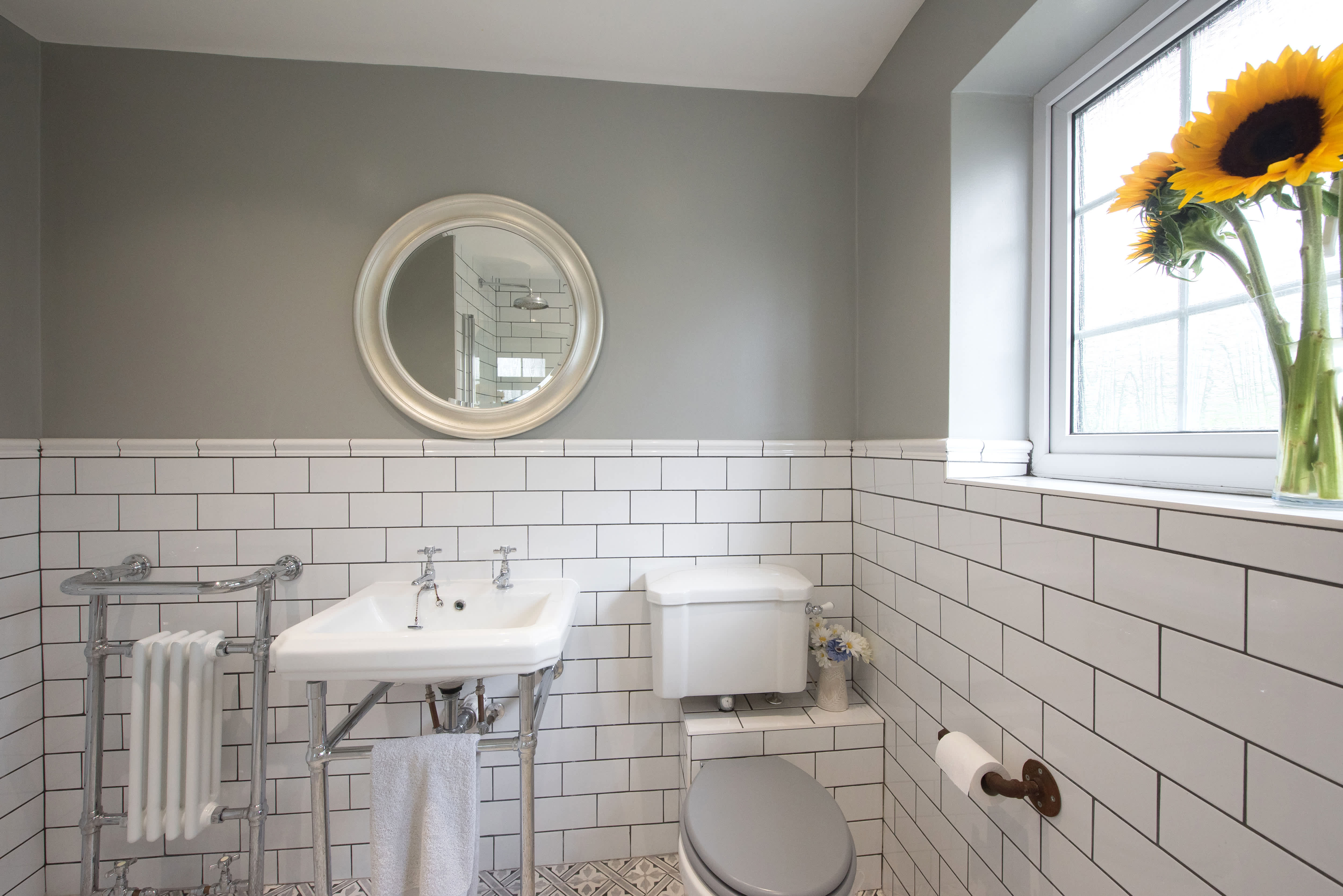 Industrial vessel bathroom sink on wood vanity below industrial pendant lamp and three mirrors
