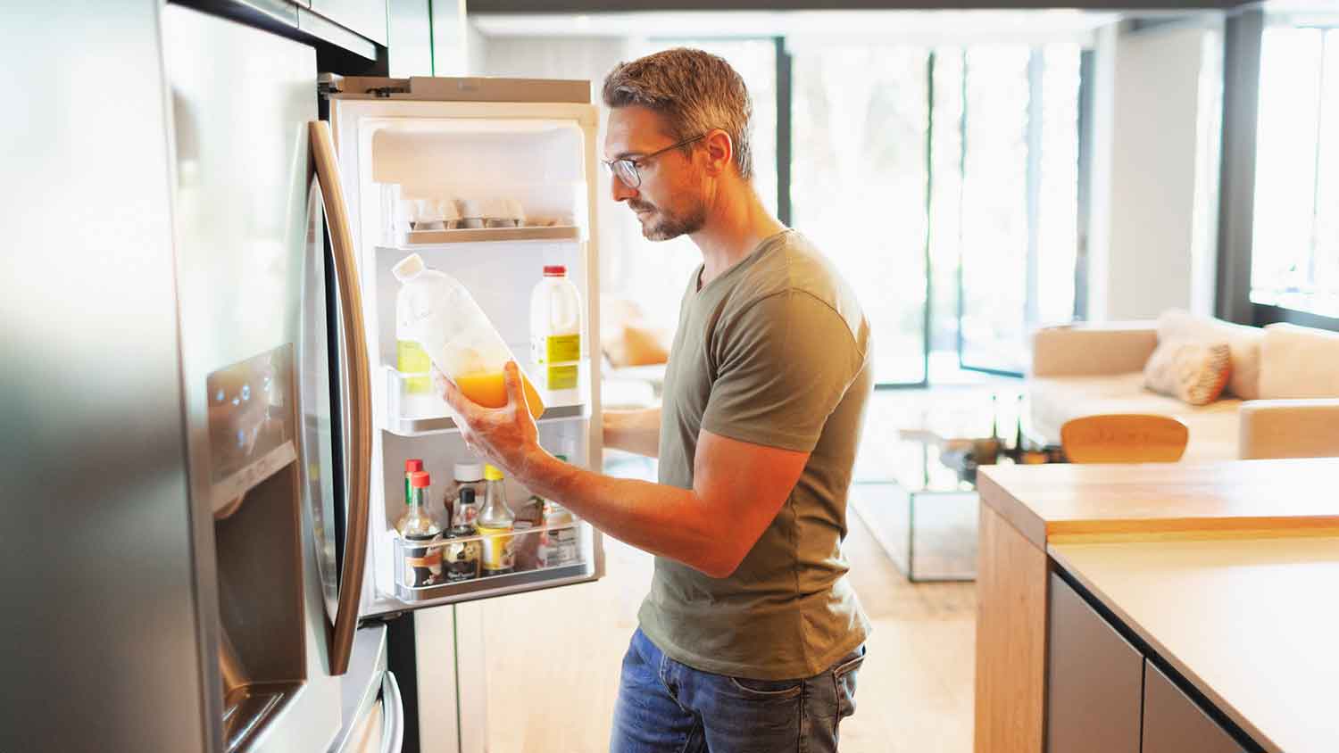 Man opening refrigerator and holding orange juice