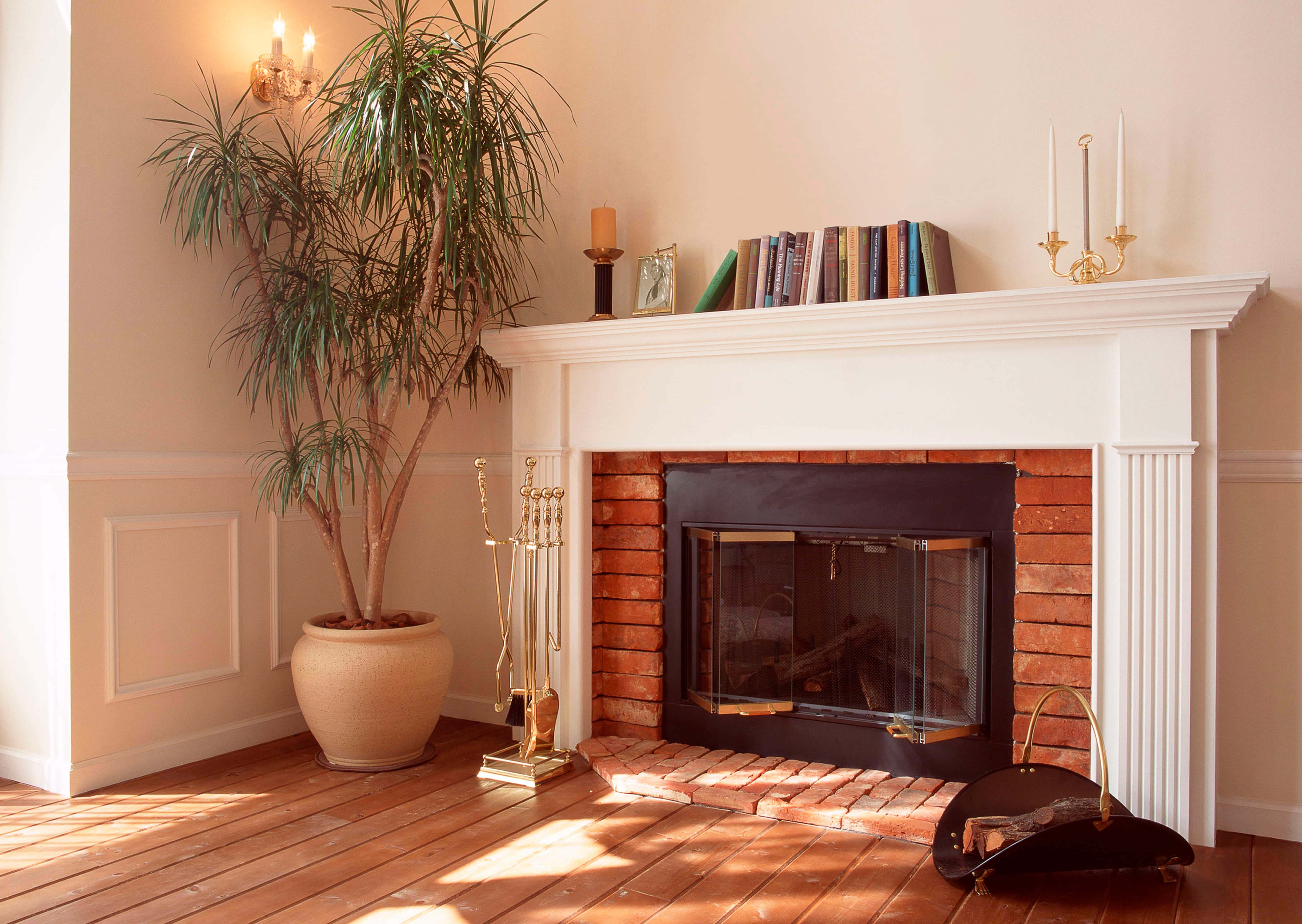 Red exposed brick fireplace and white mantel with books on top, plus gold fireplace tools