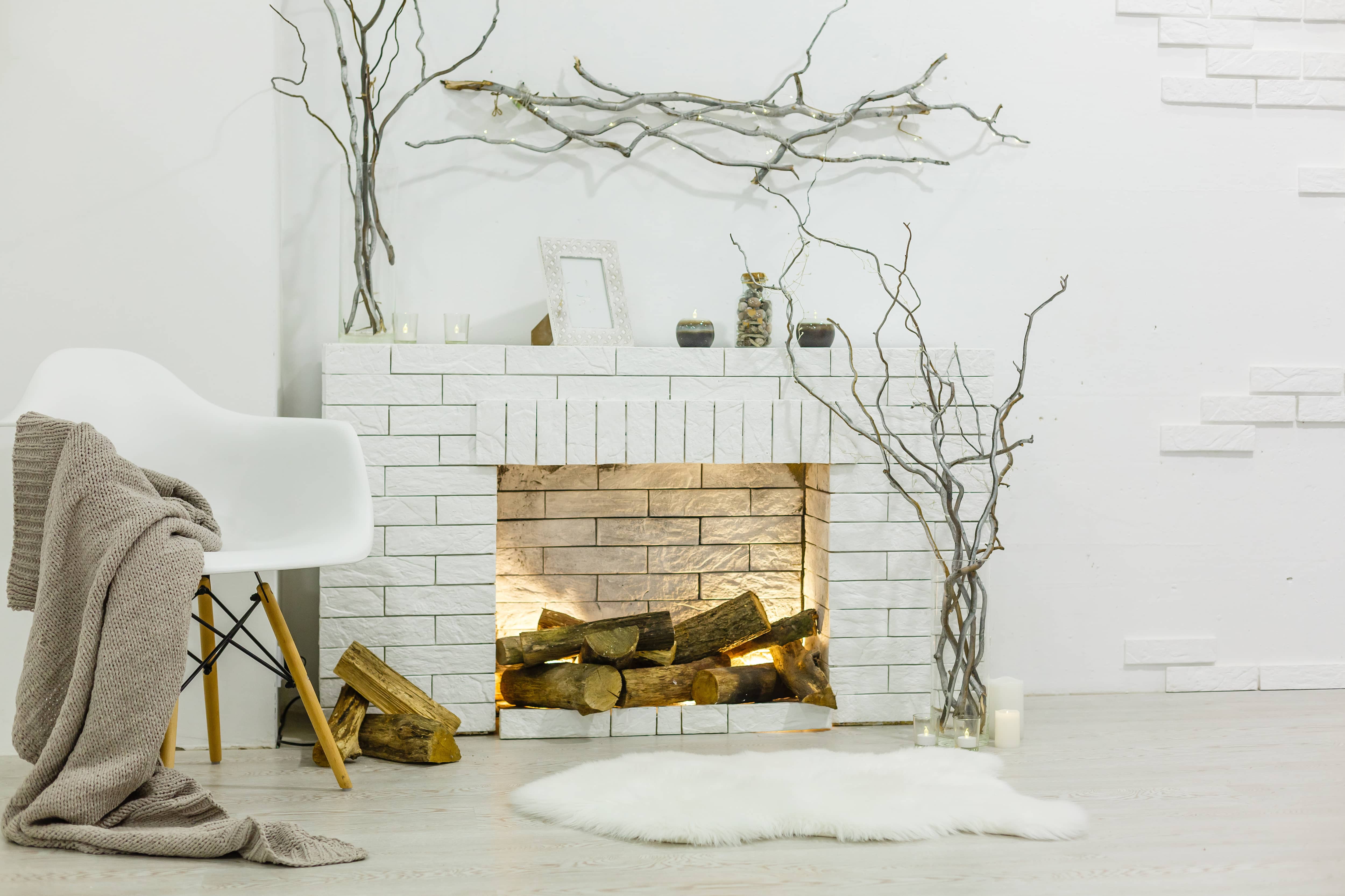 White brick fireplace with lights and logs and mantel with stick decorations in a white room
