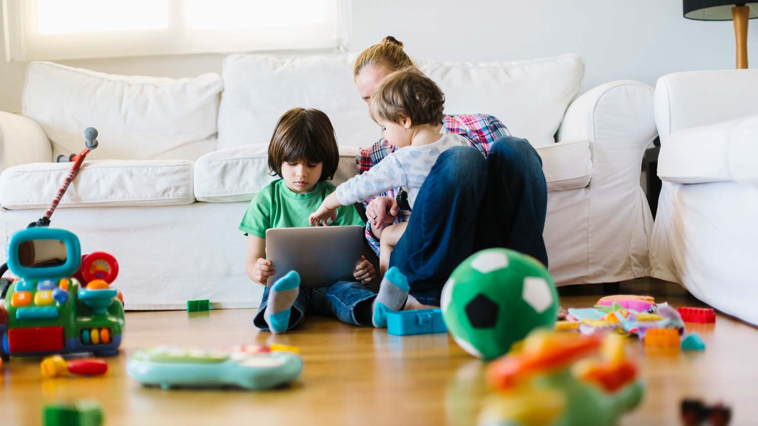 A mother with her two kinds using a tablet while sitting on laminate floor