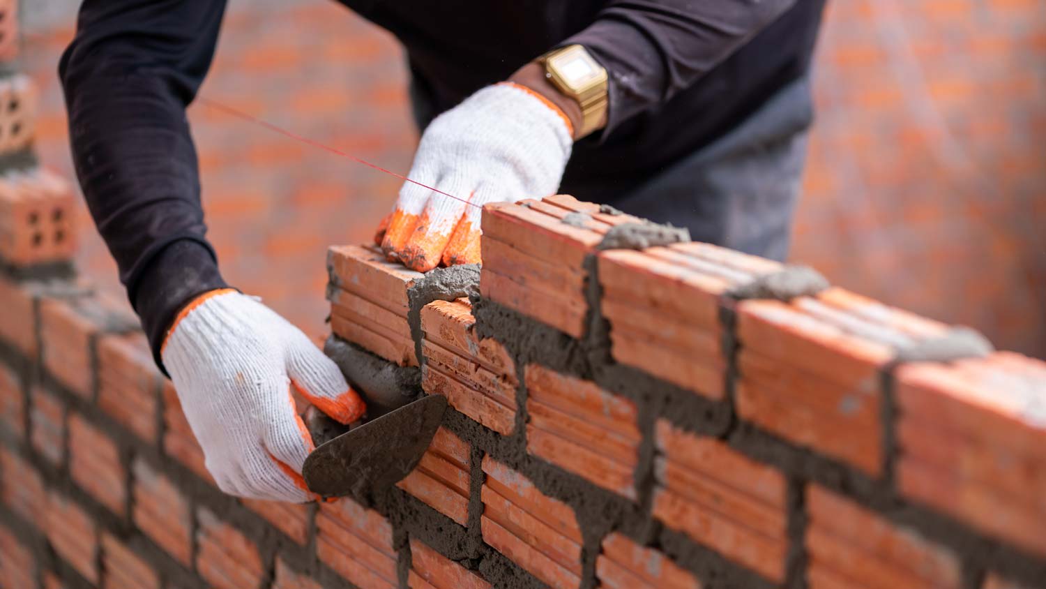 A worker’s hand installing brick at a construction site