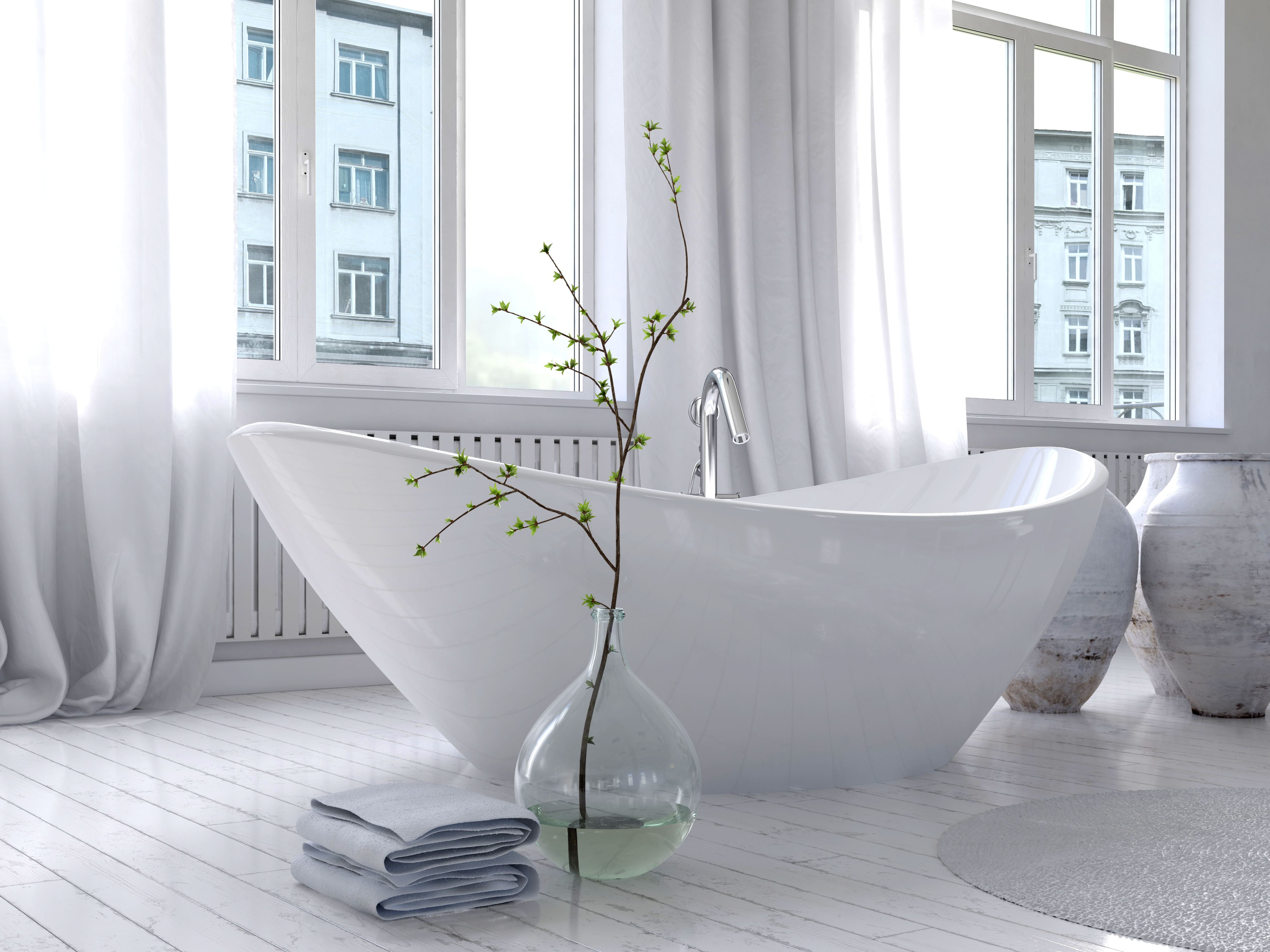 All white bathroom with freestanding white bathtub next to large teardrop vase holding budding branch