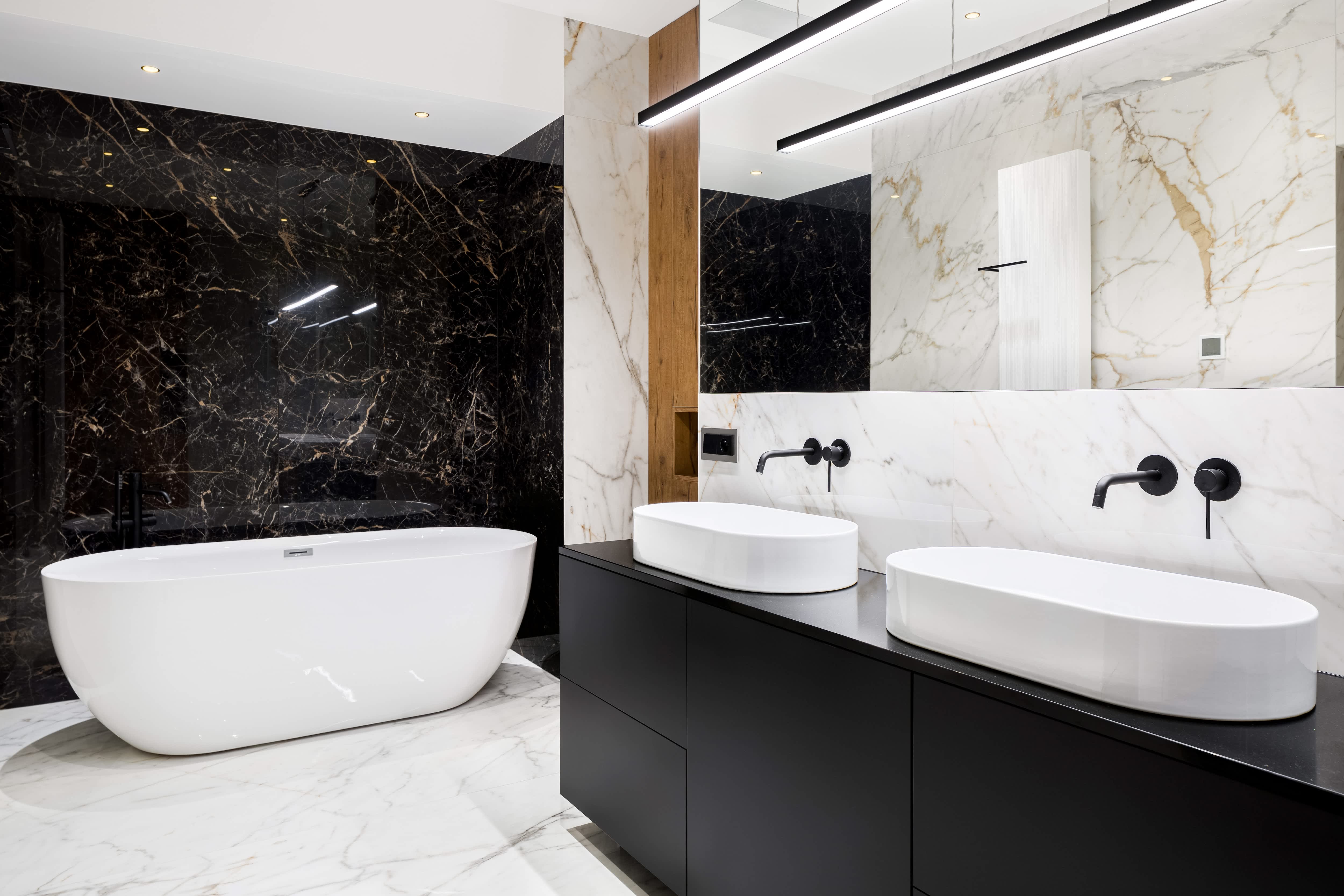 Luxury bathroom with black and white marble walls and floor, black vanity, and freestanding white tub