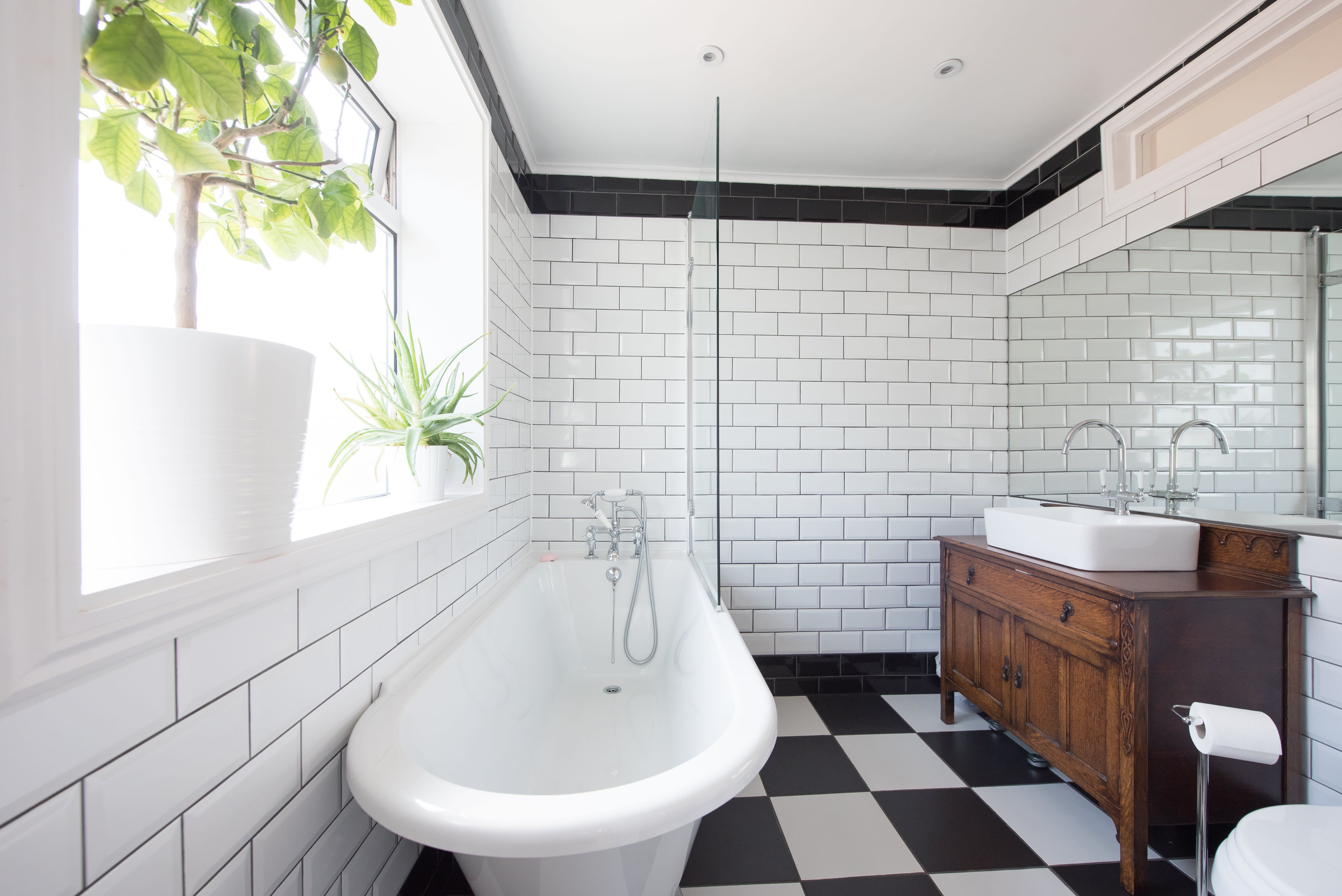 Art deco bathroom with roll-top tub, black and white subway tiles, black-and-white checked floor, and vessel sink on brown vanity