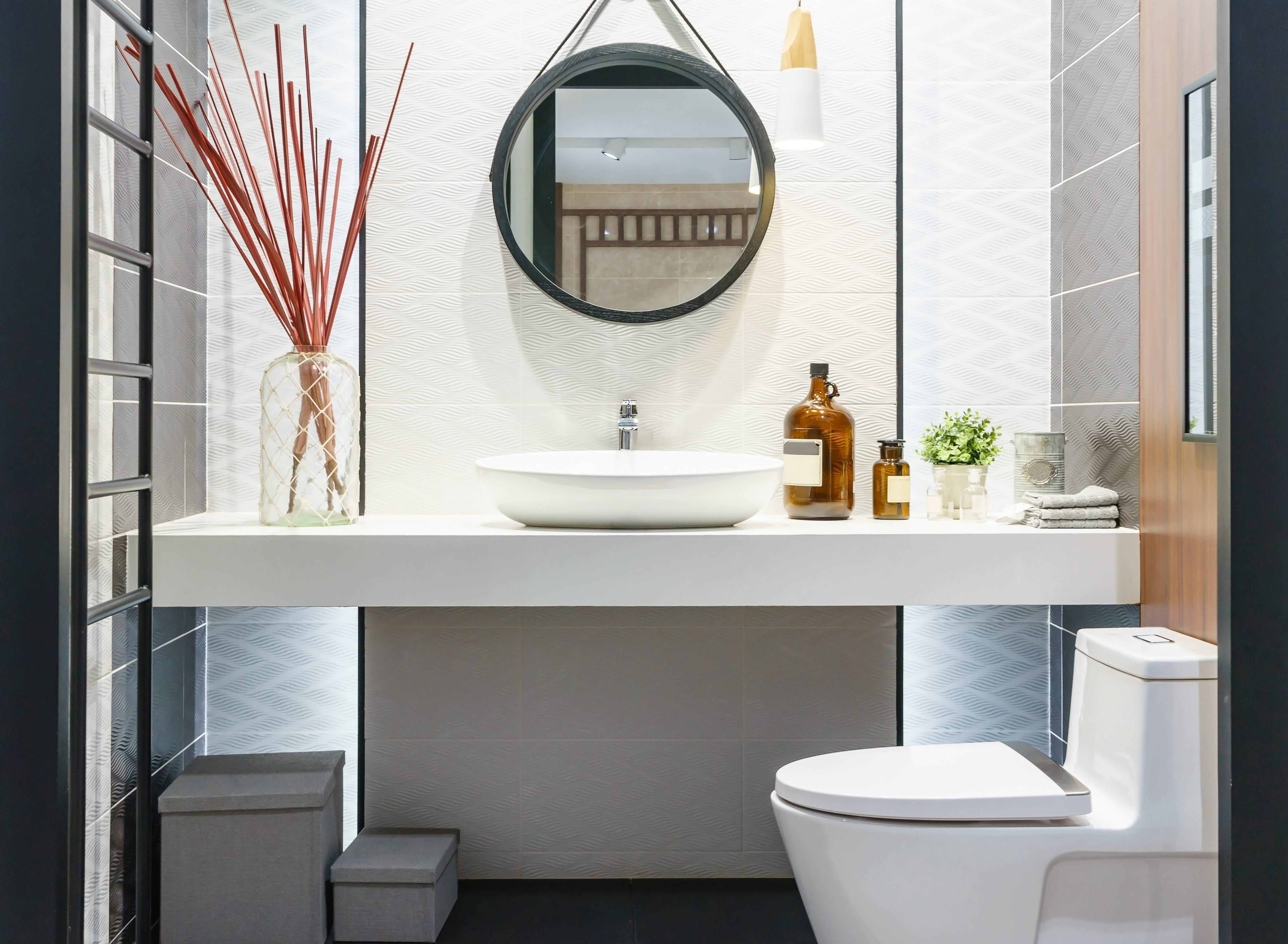 Modern bathroom with vessel sink, white and black tiles, black ladder towel rack, and black circle mirror
