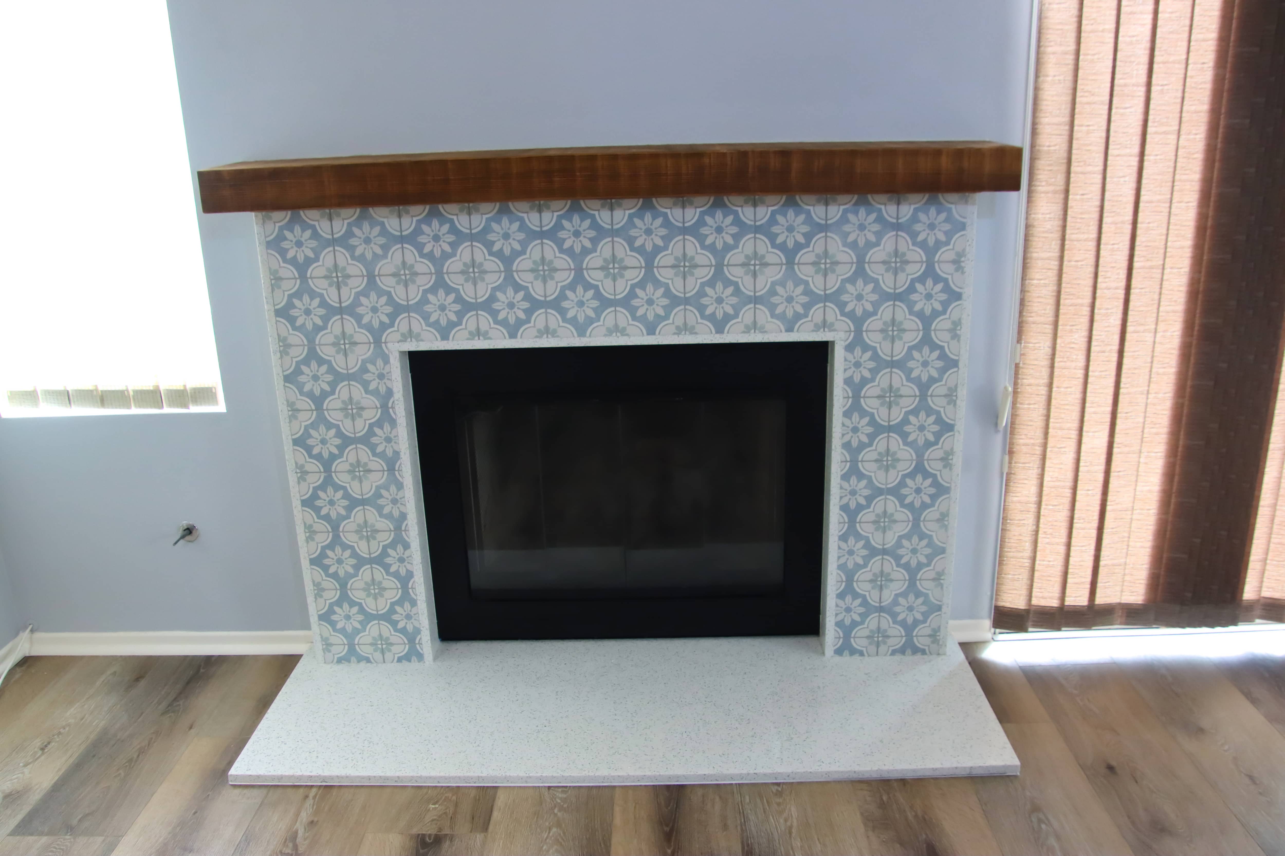 Fireplace with brown wood mantel and patterned tile featuring white flowers on a light blue background