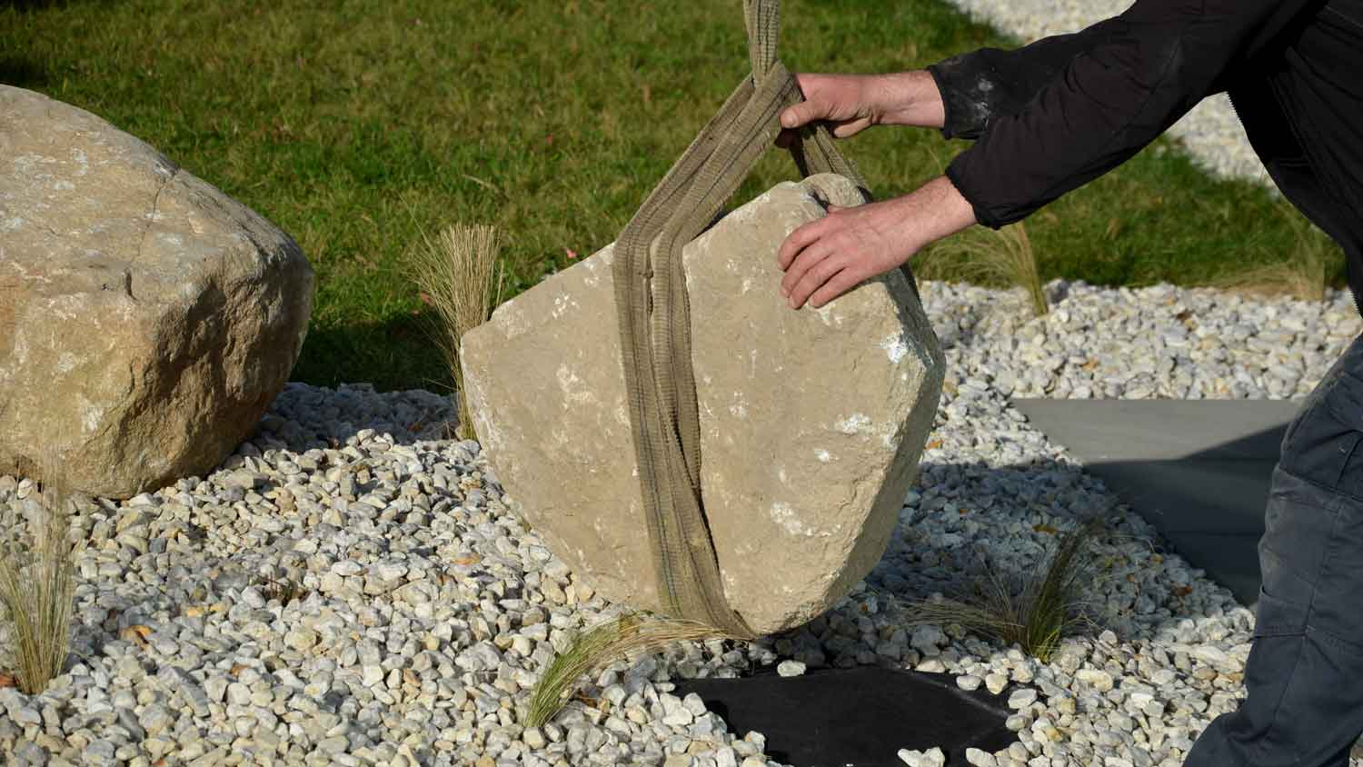 A man removing a boulder from a landscaped yard