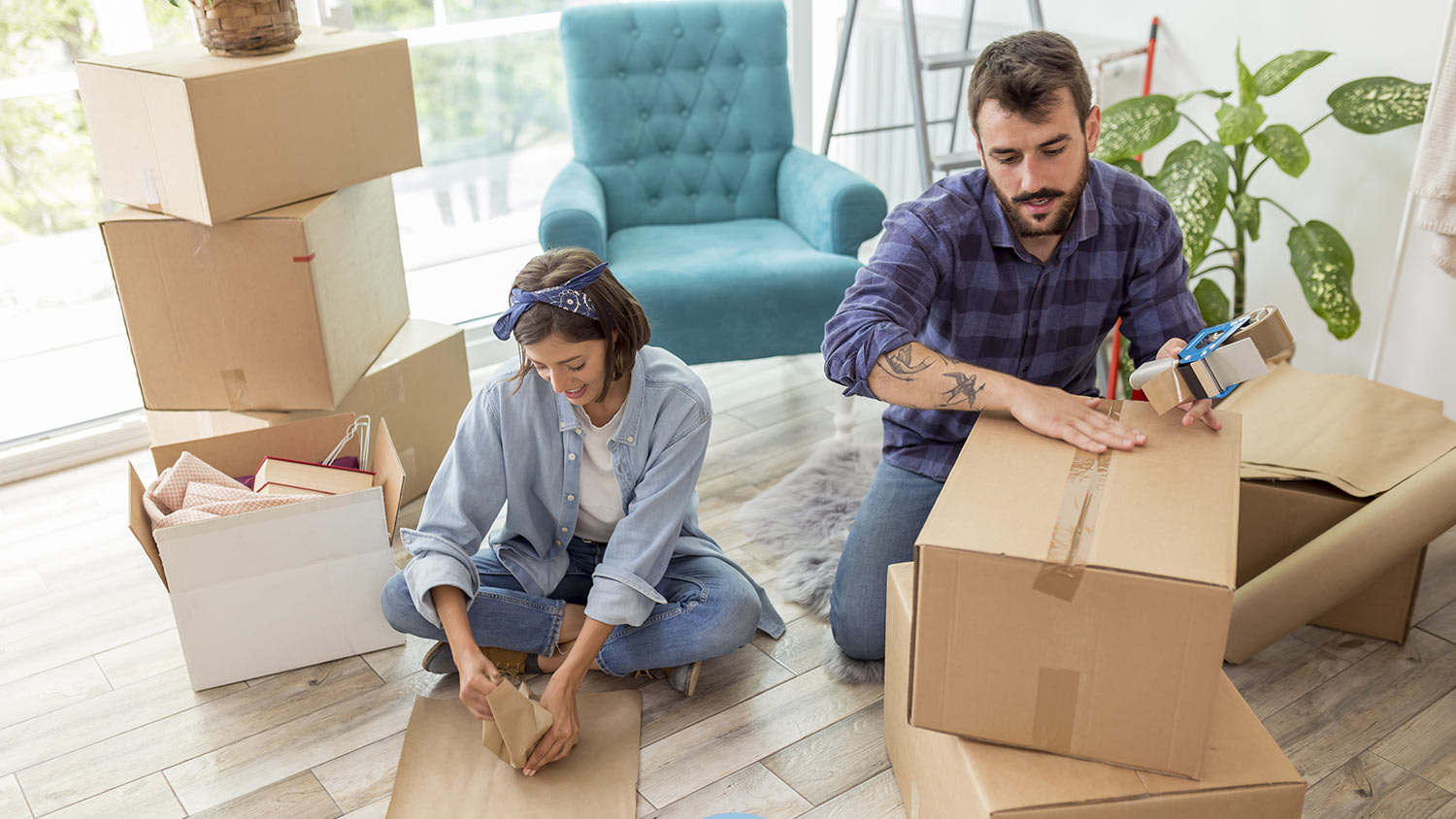 Husband and wife tape up moving boxes in home