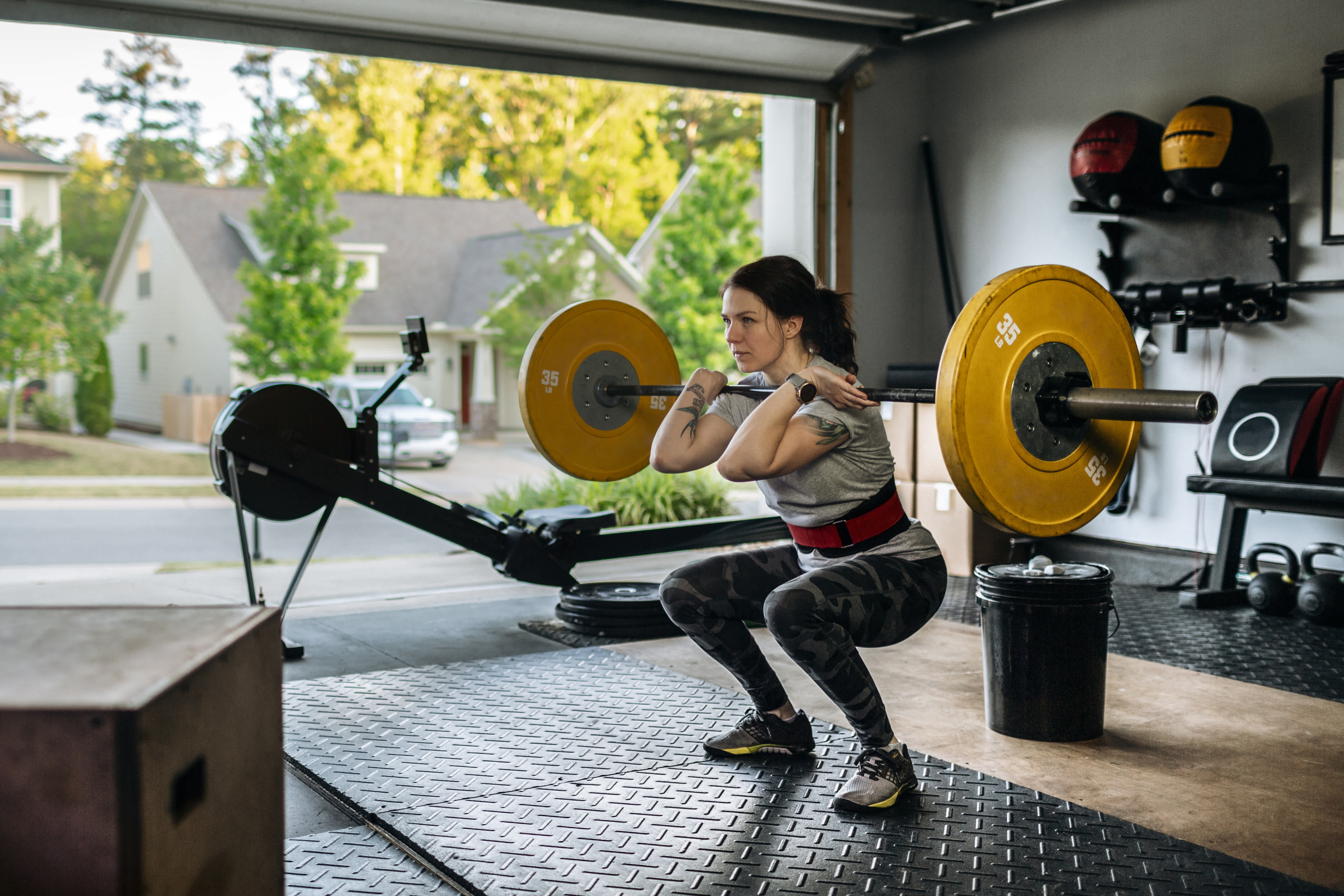 Young woman in gym clothes weight lifting in her garage home gym surrounded by gym equipment