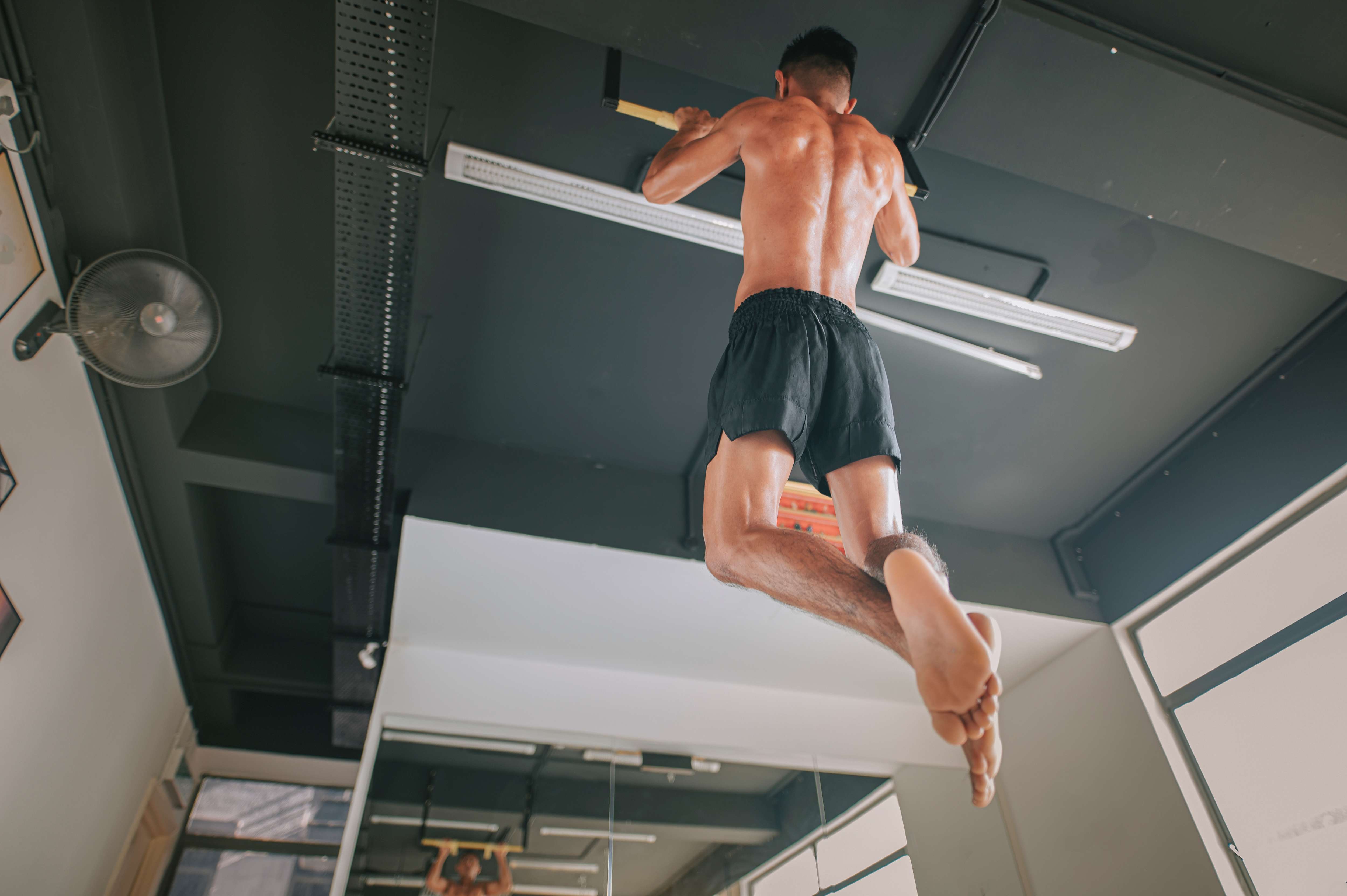 Man doing pull ups in his garage home gym facing a mirror with a fan in the upper left hand corner