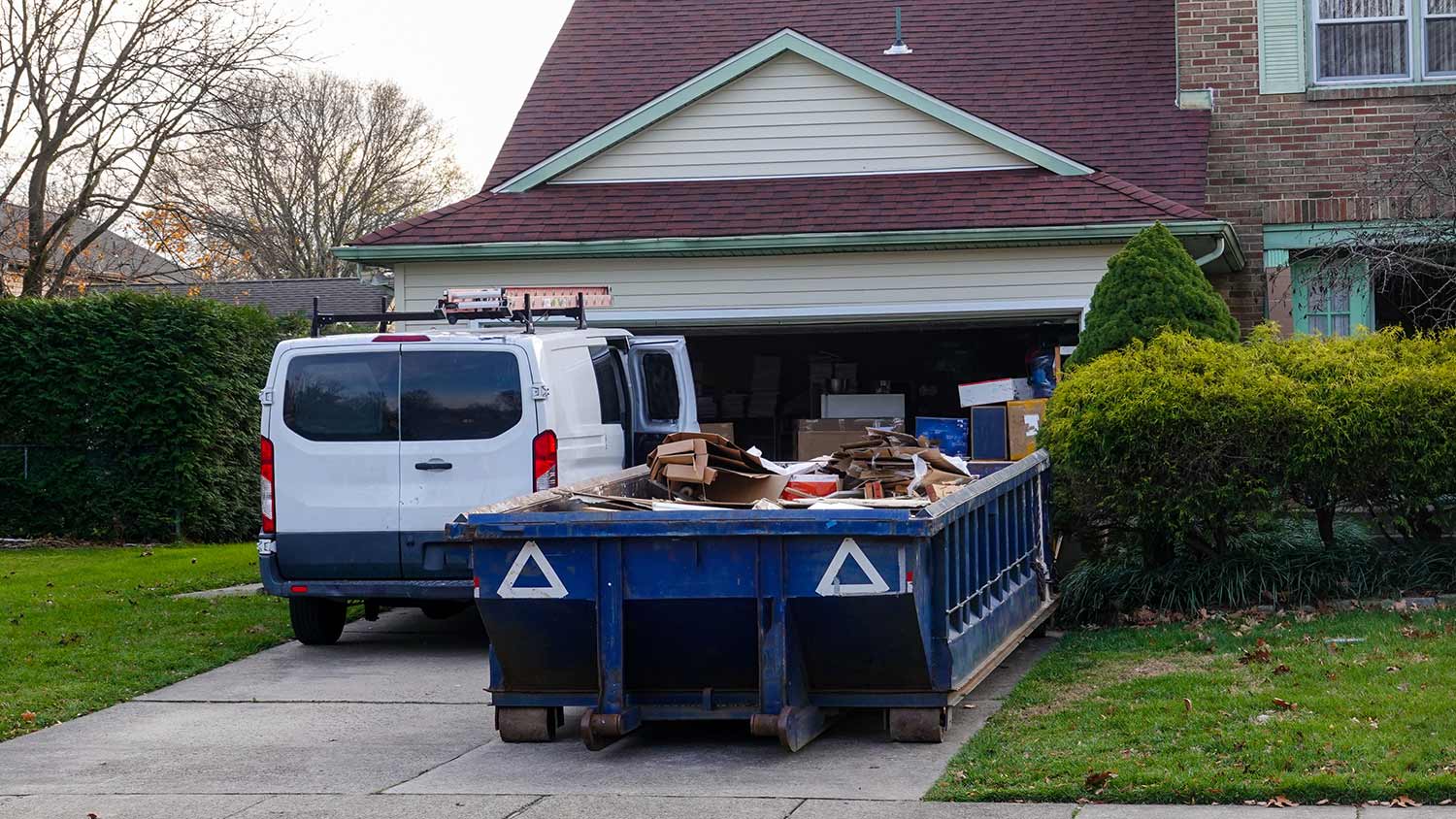 Dumpster full of cardboard and construction debris in front of a garage