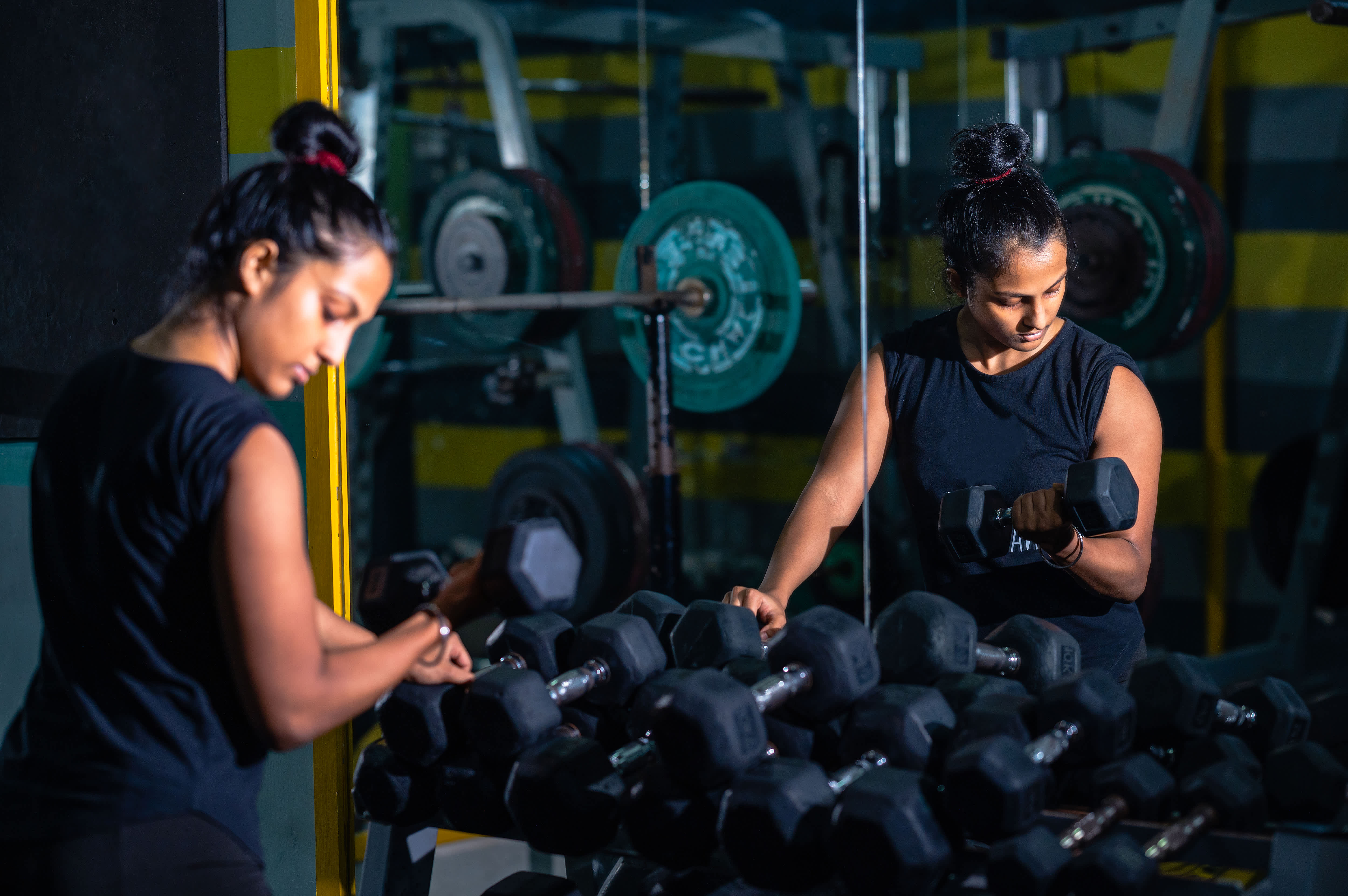 Woman leaning on weight rack with a dumbbell in her right hand doing a curl facing a large mirror in her garage home gym
