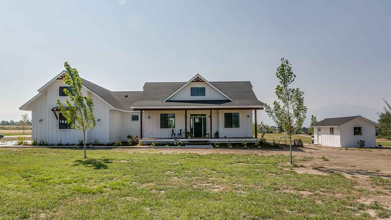 A white farmhouse with small trees on the front yard