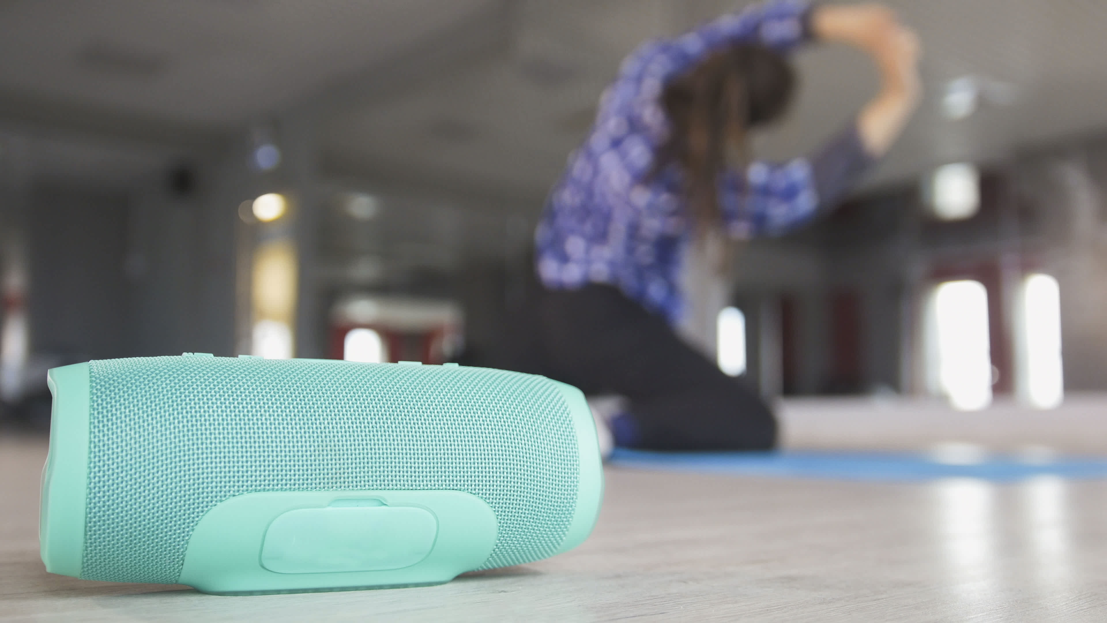 A woman stretching on the floor of her home gym with a turquoise wireless speaker