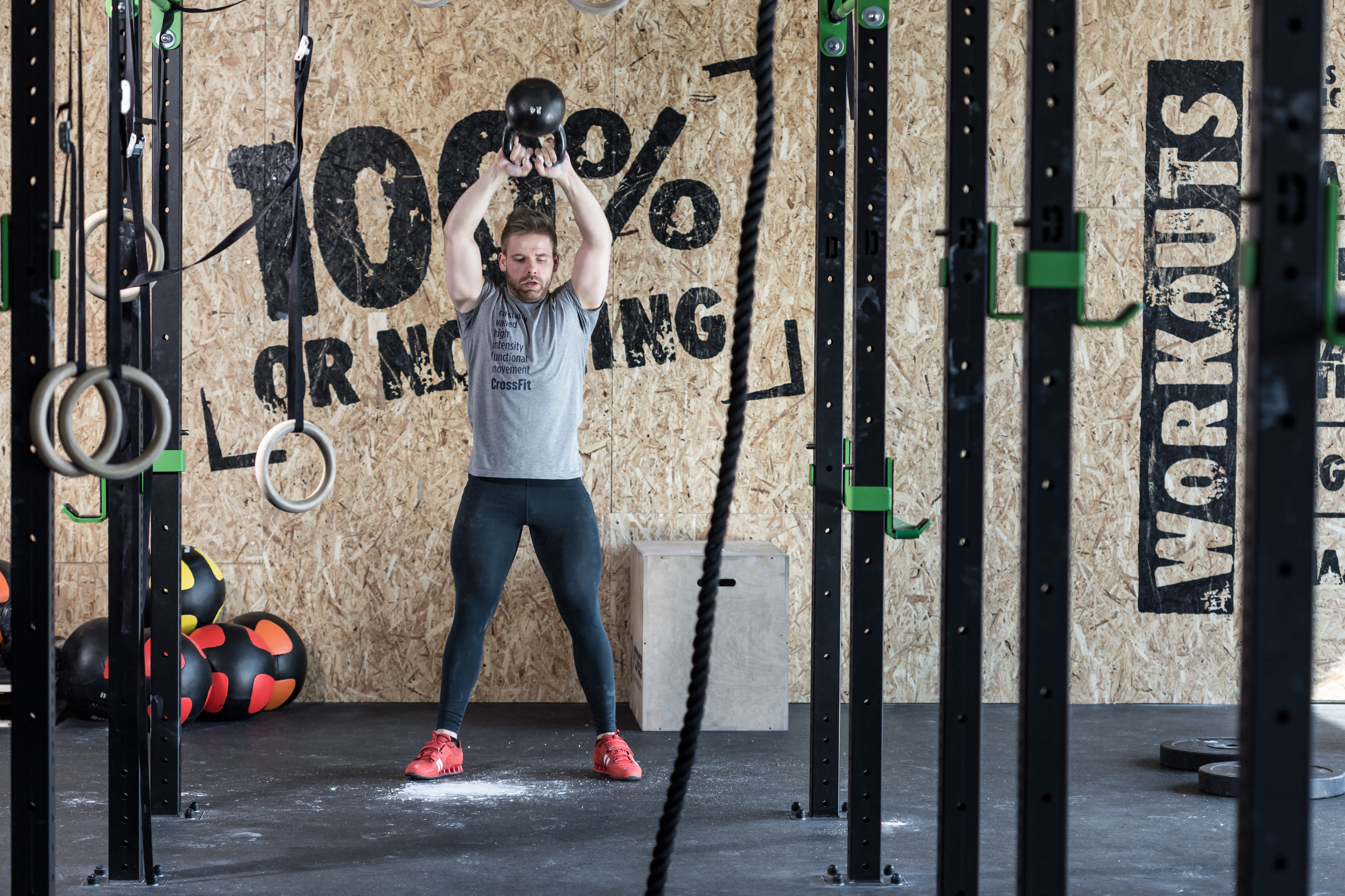 Man in gym clothes working out with a kettlebell in a garage home gym with an inspirational quote painted on the wall behind him