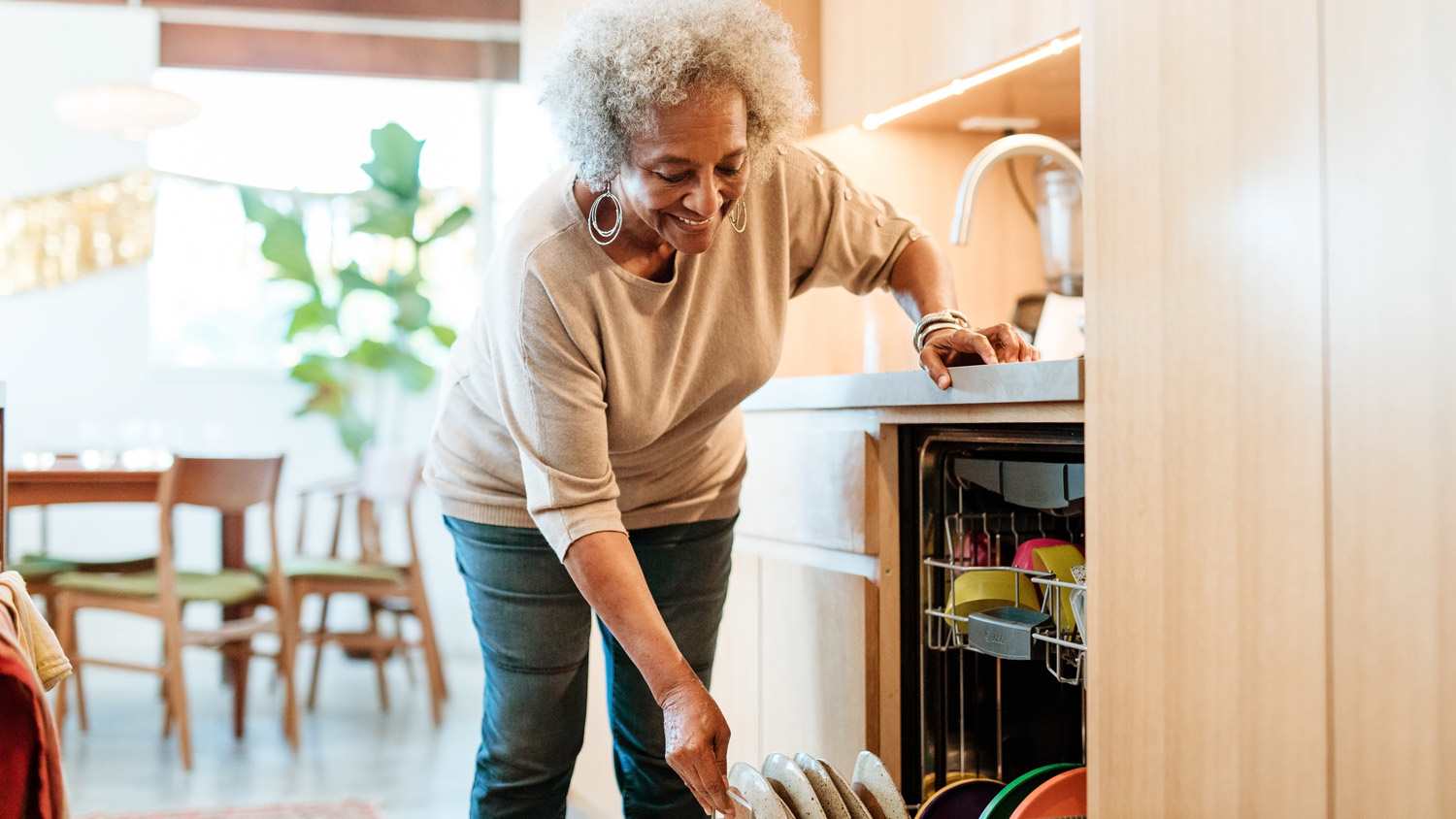 Smiling senior woman keeping plates in dishwasher