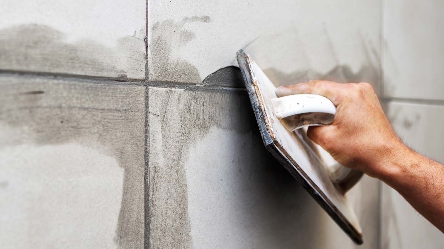 A hand laying epoxy grout on tiles