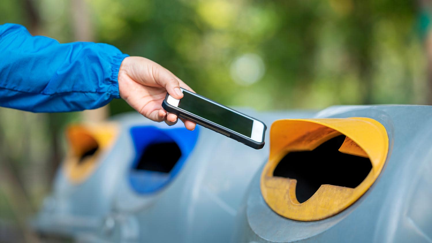 A person disposing a phone in a recycle bin