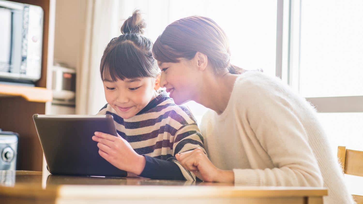 A mother and her daughter playing with an electronic device