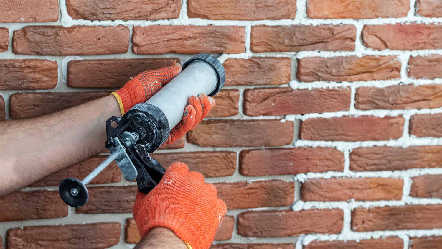 A person filling cement grout on faux bricks