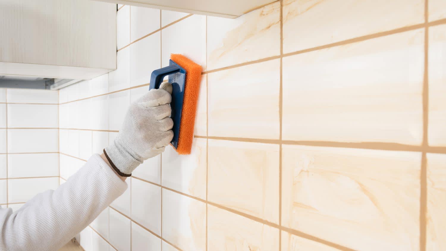 A person wiping excessive epoxy grout from tiles