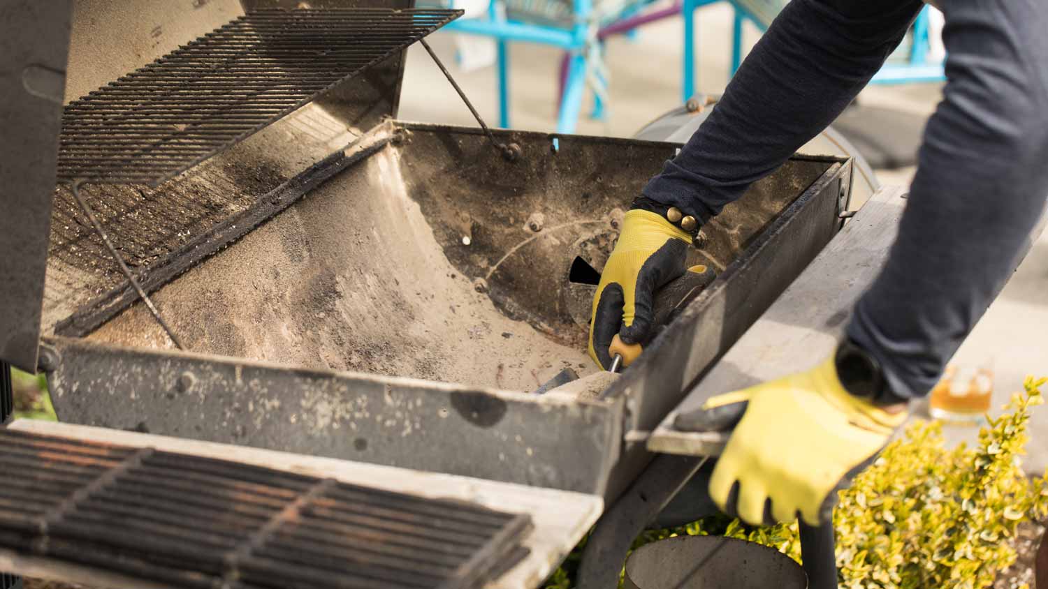 A person cleaning a barbeque by removing ashes