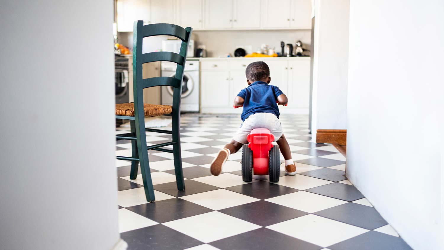 A kid riding a tricycle in the kitchen