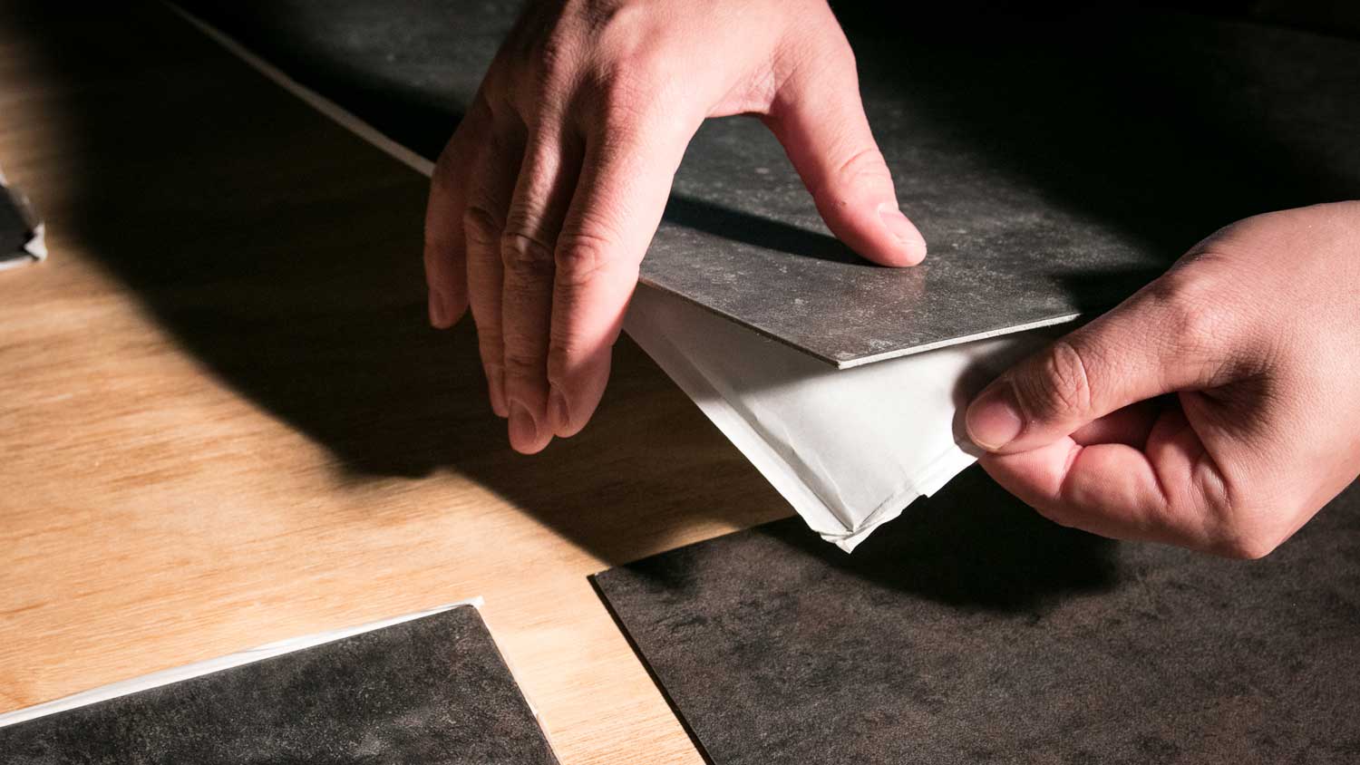 A person removing back from peel and stick tiles